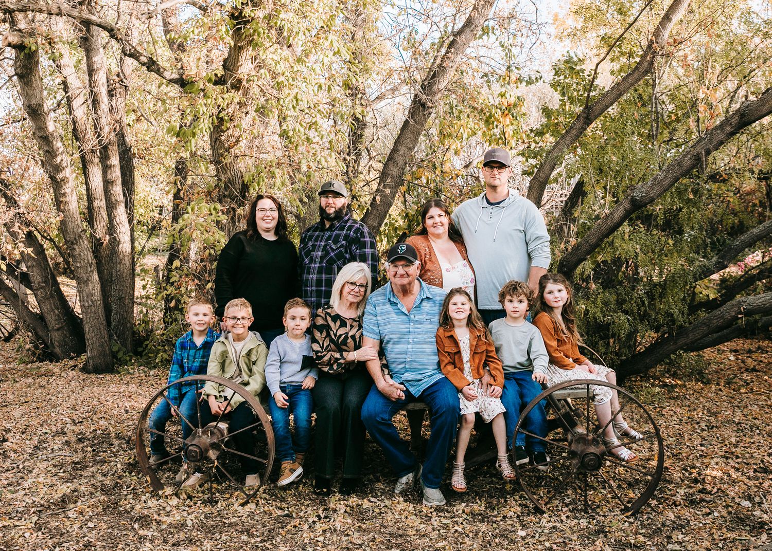 A large multigenerational family poses together outdoors among autumn trees.