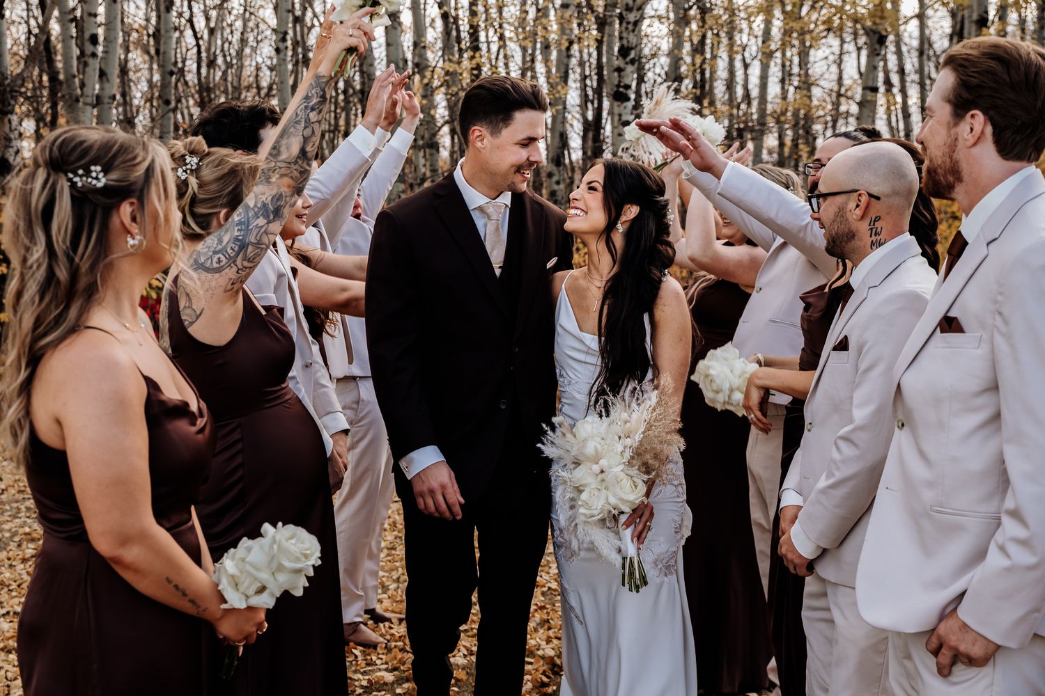 A bride and groom stand together surrounded by their wedding party in a beautiful autumn forest setting.