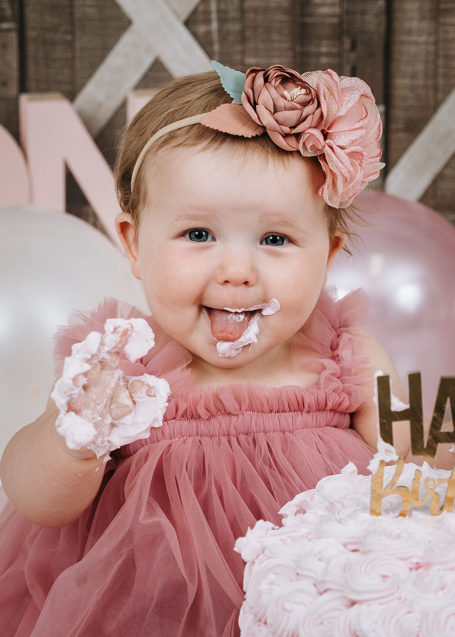Adorable baby girl in pink tutu dress with floral headband enjoying first birthday cake smash.