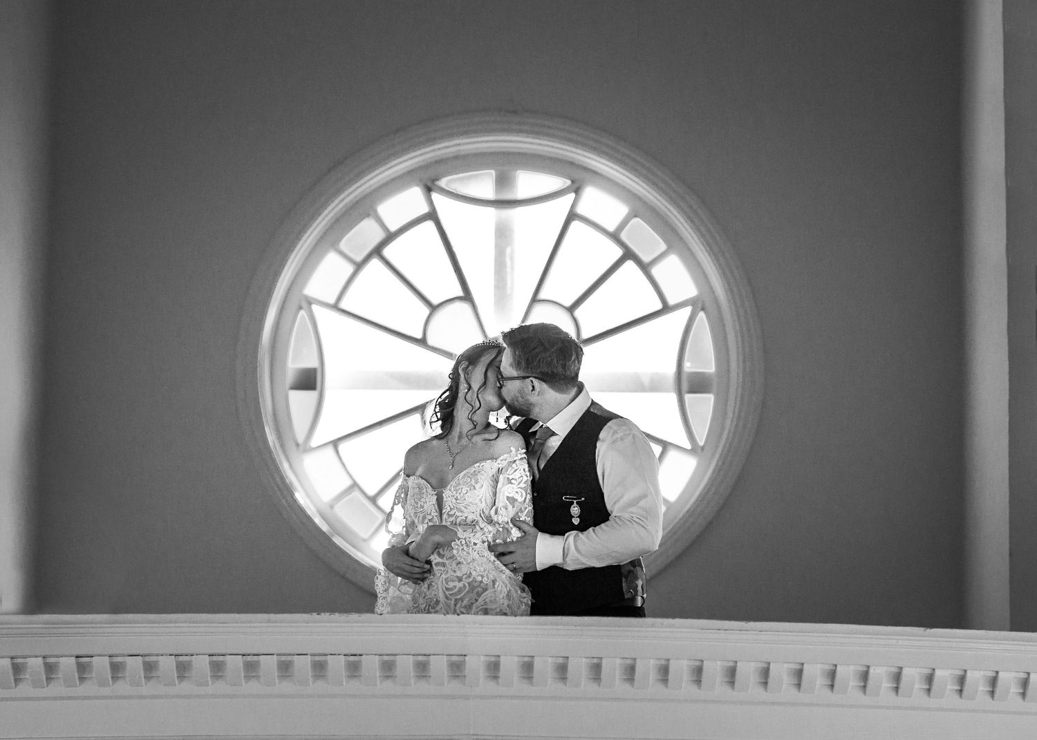 Black and white romantic wedding portrait of couple kissing in front of a stunning circular stained glass window.