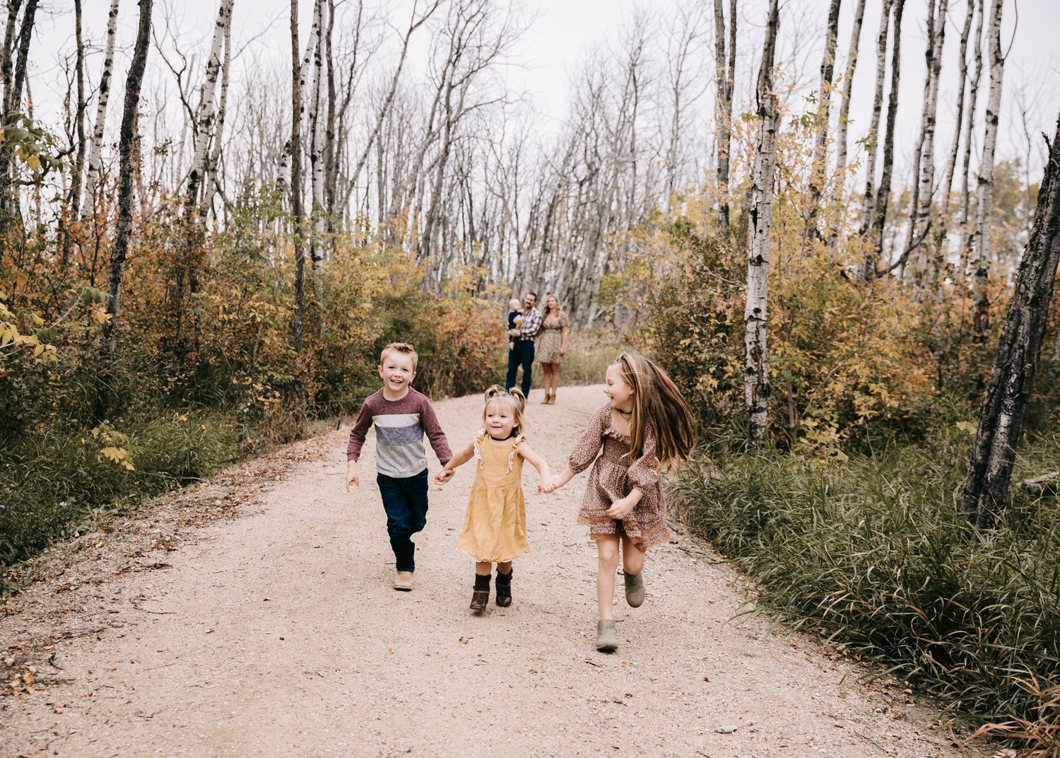 Three joyful children running hand-in-hand down a scenic autumn forest trail together.