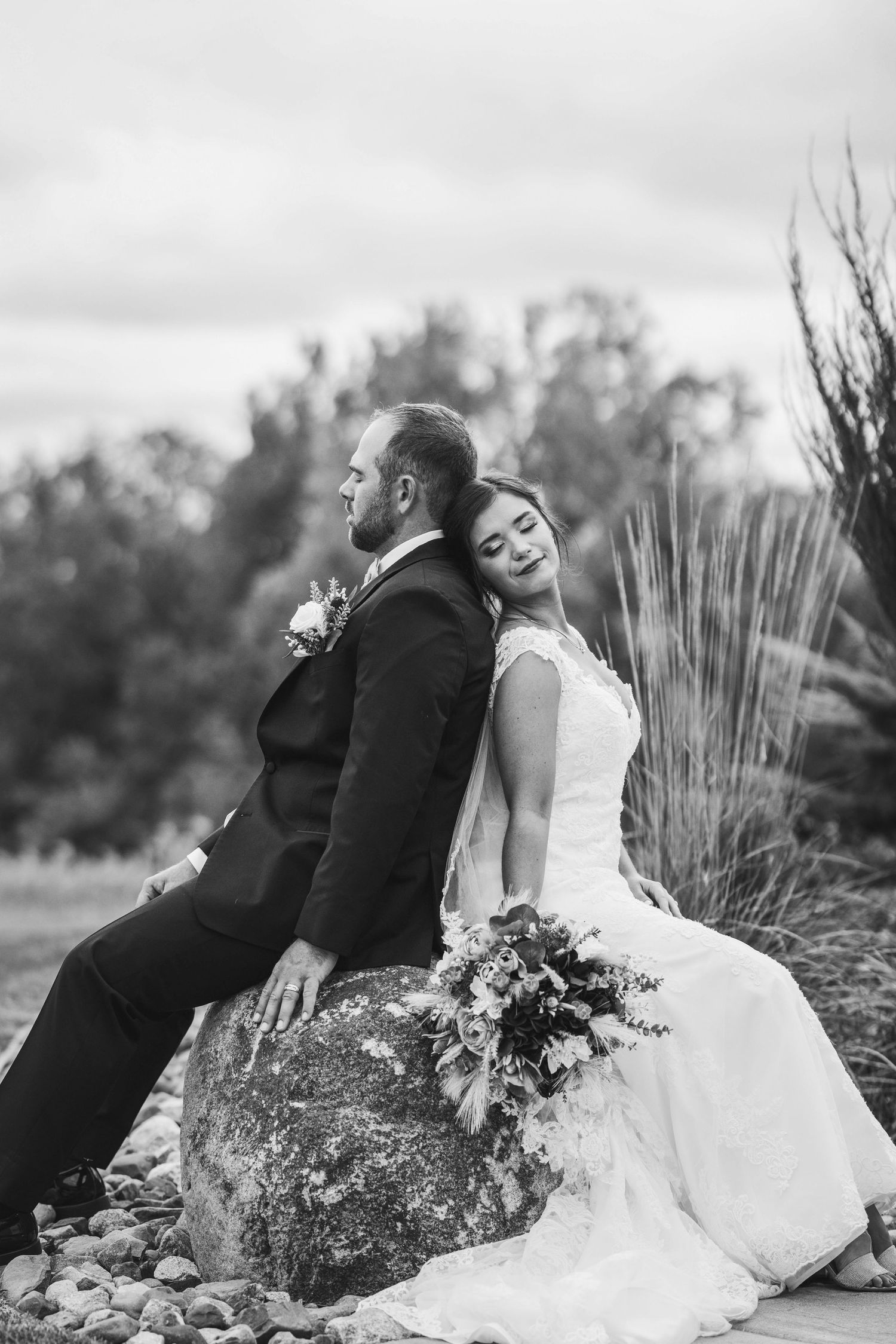 A romantic black and white wedding photo series shows a couple sitting together on rocks outdoors in nature.