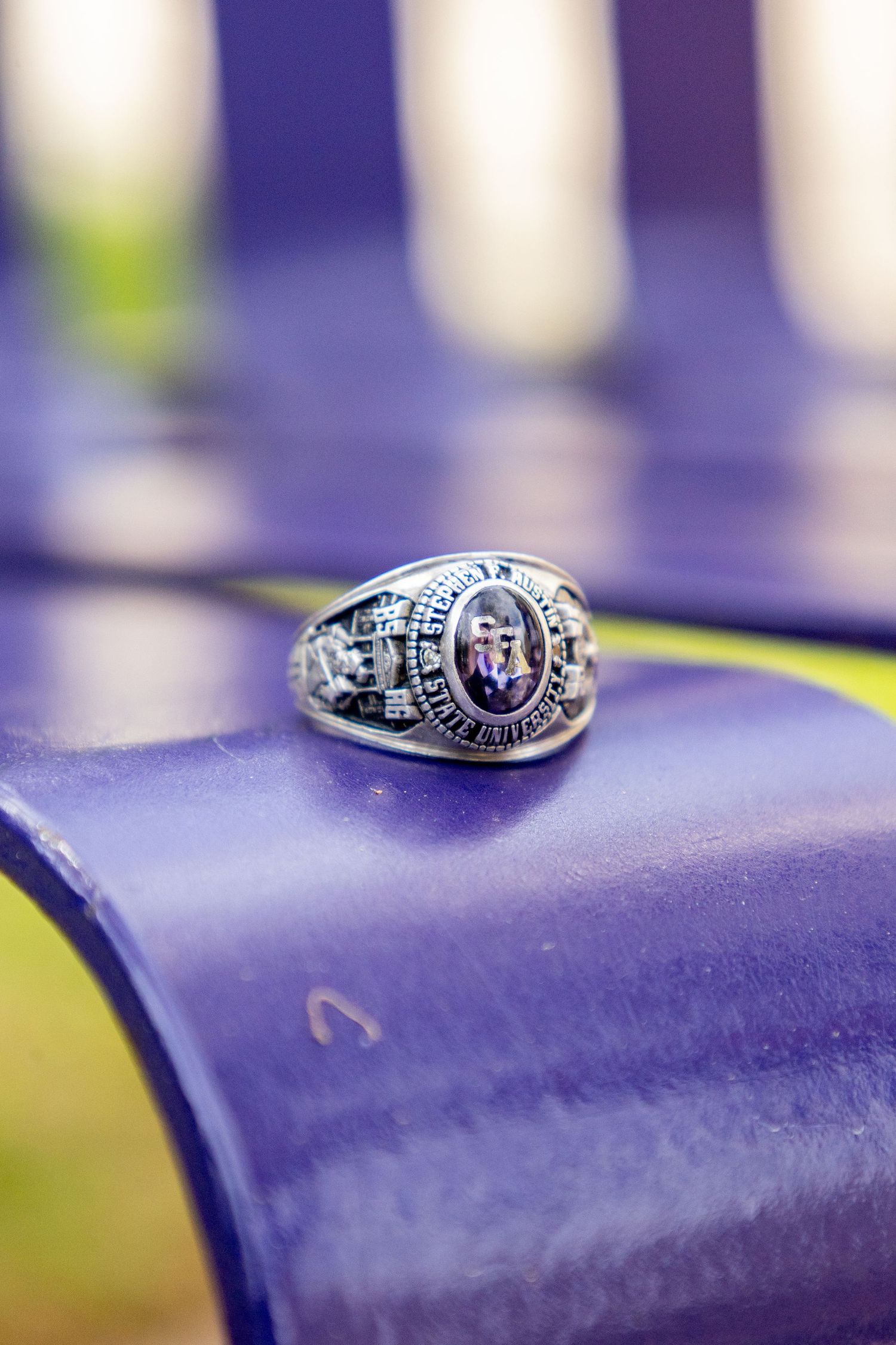 Silver class ring with purple gemstone resting on a purple metal chair, symbolizing academic achievement.