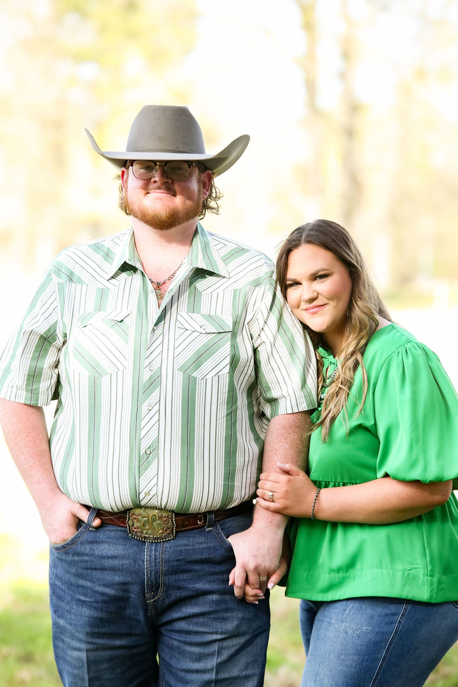 Couple in western wear with striped shirts and green blouse posing outdoors.