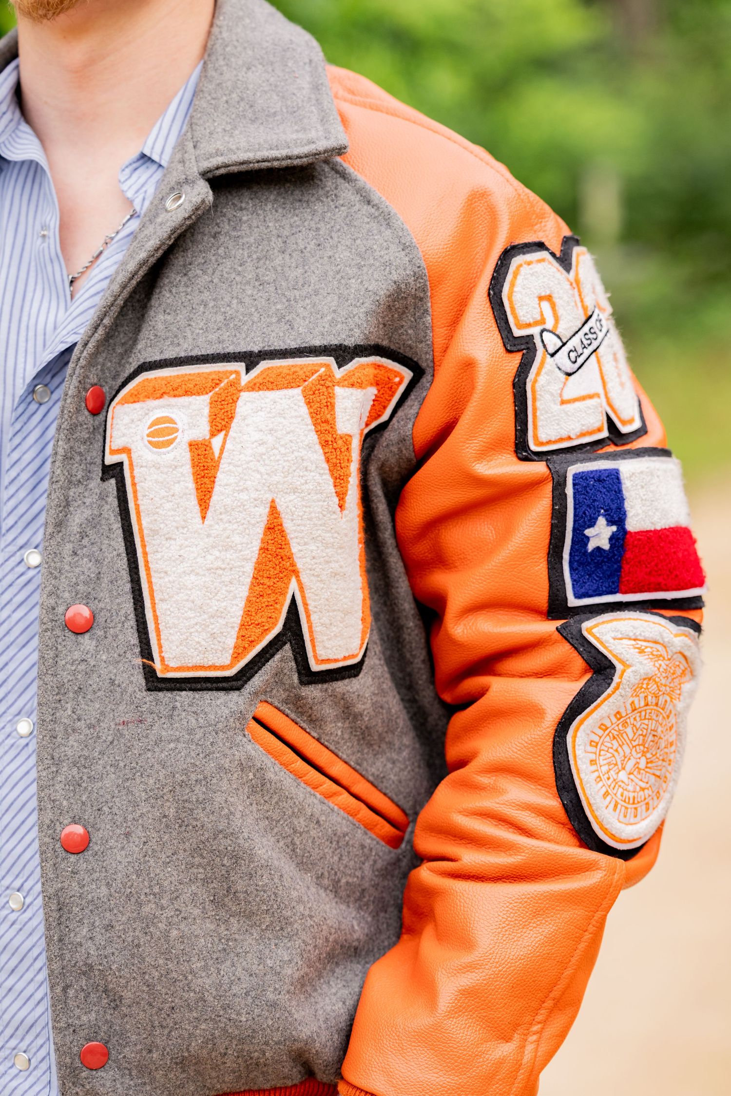 Gray and orange varsity letterman jacket with W patch, Texas flag badge, and leather sleeves on a male student.