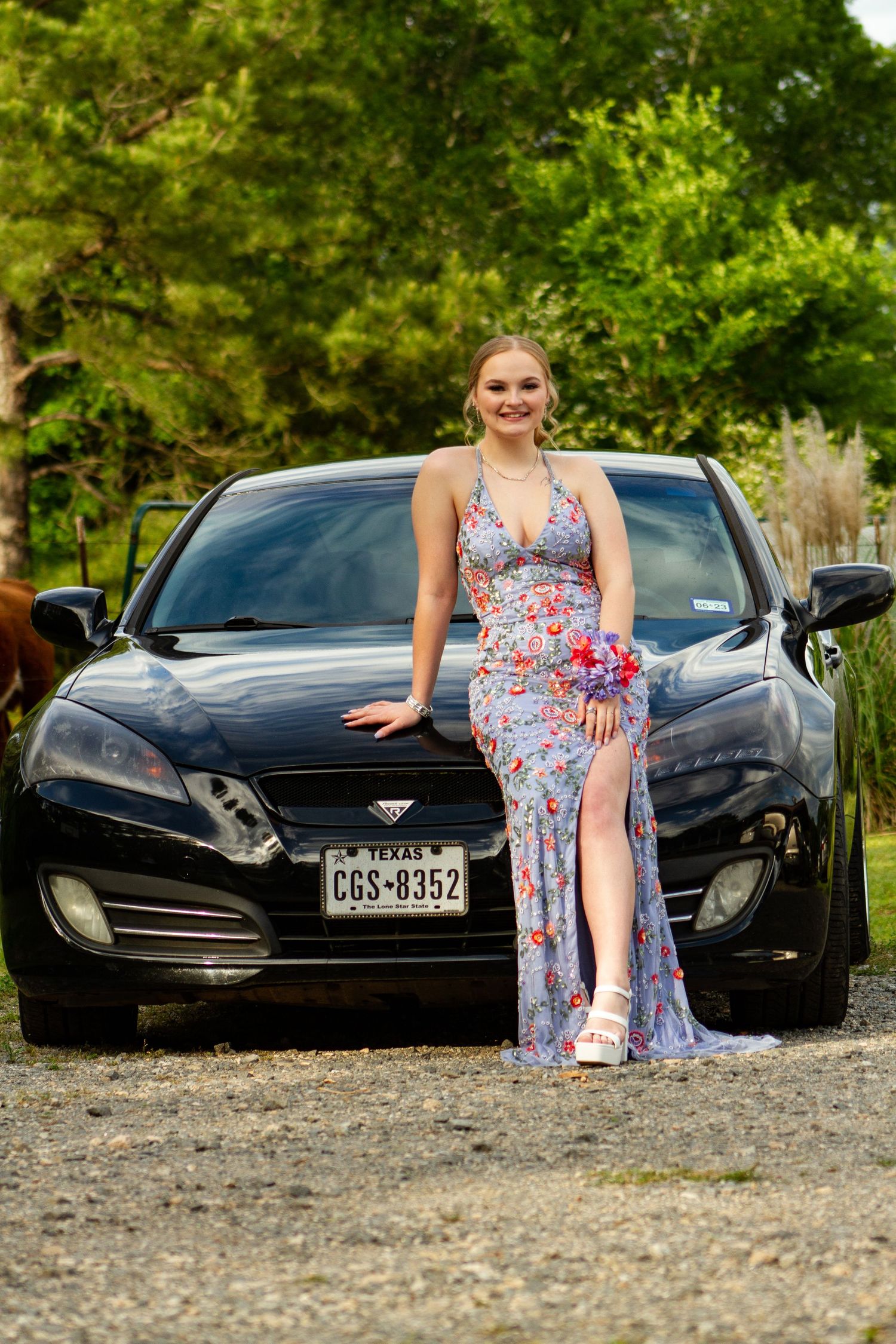 Stylish outdoor photoshoot featuring a floral dress and black sports car.