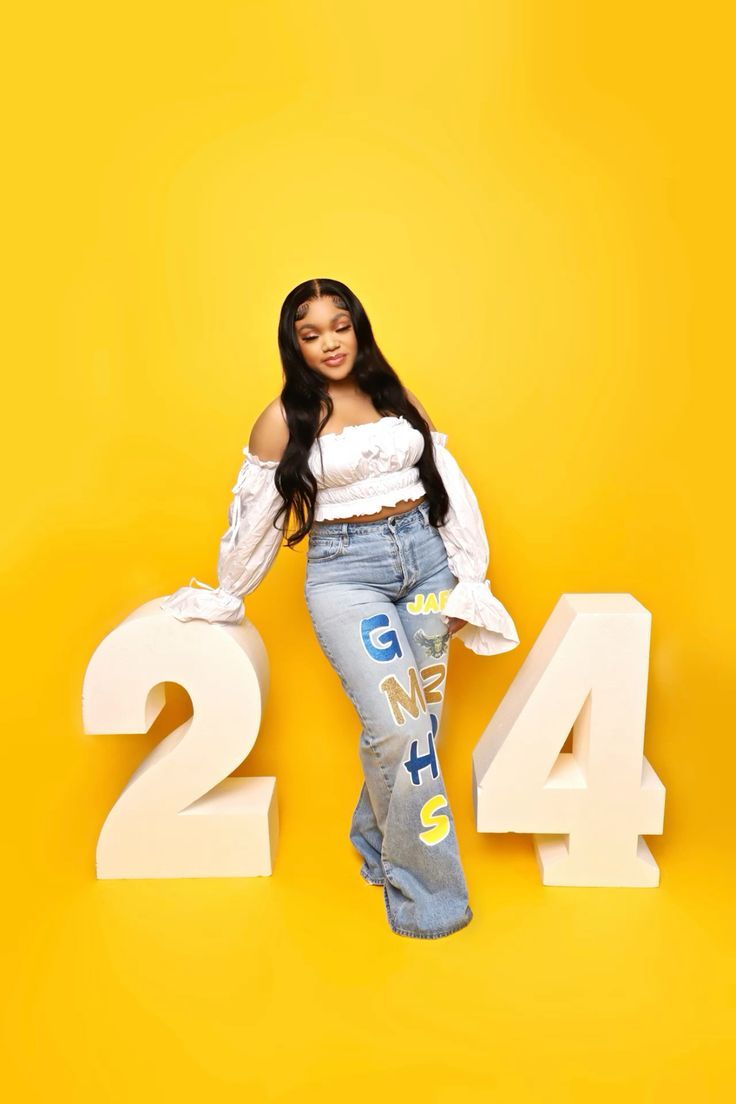 Trendy fashion photo with decorative numbers 2 and 4 on bright yellow background featuring white top and patterned jeans.