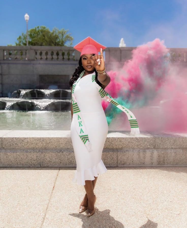 Graduation celebration photo with pink smoke effect near a stone fountain on a sunny day.