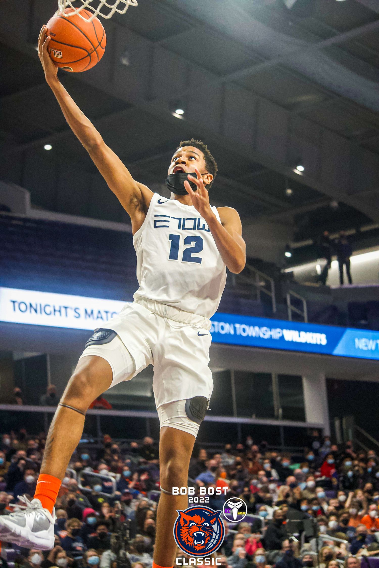 Basketball player in white jersey number 12 making athletic layup during game.