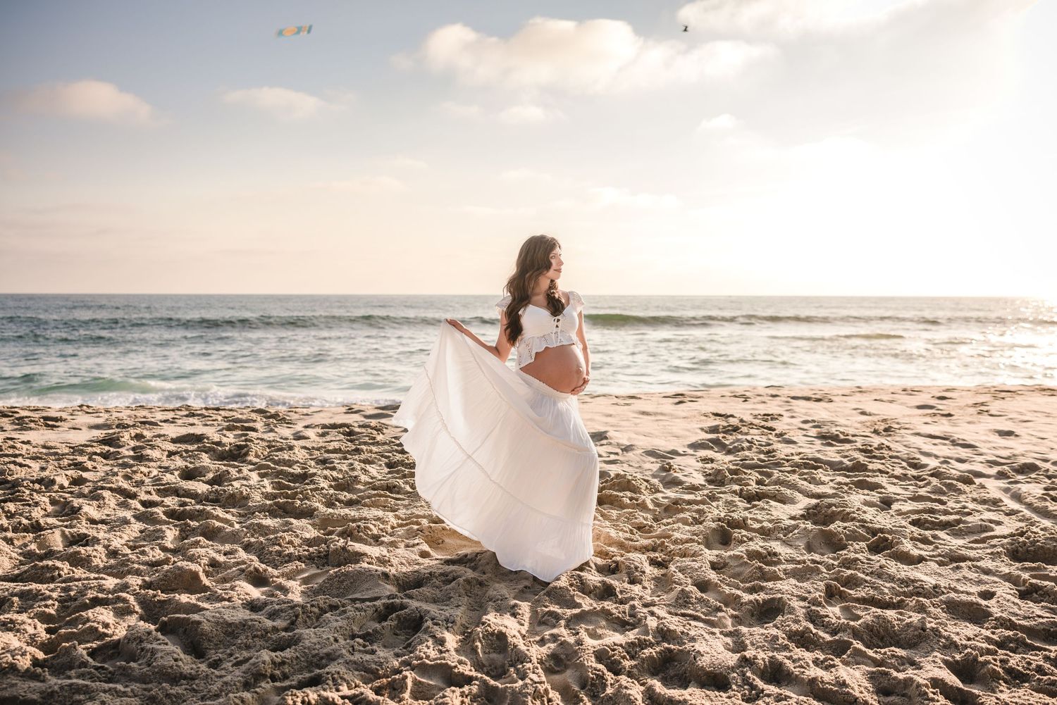A romantic beachside photoshoot featuring white dress against ocean waves at sunset.