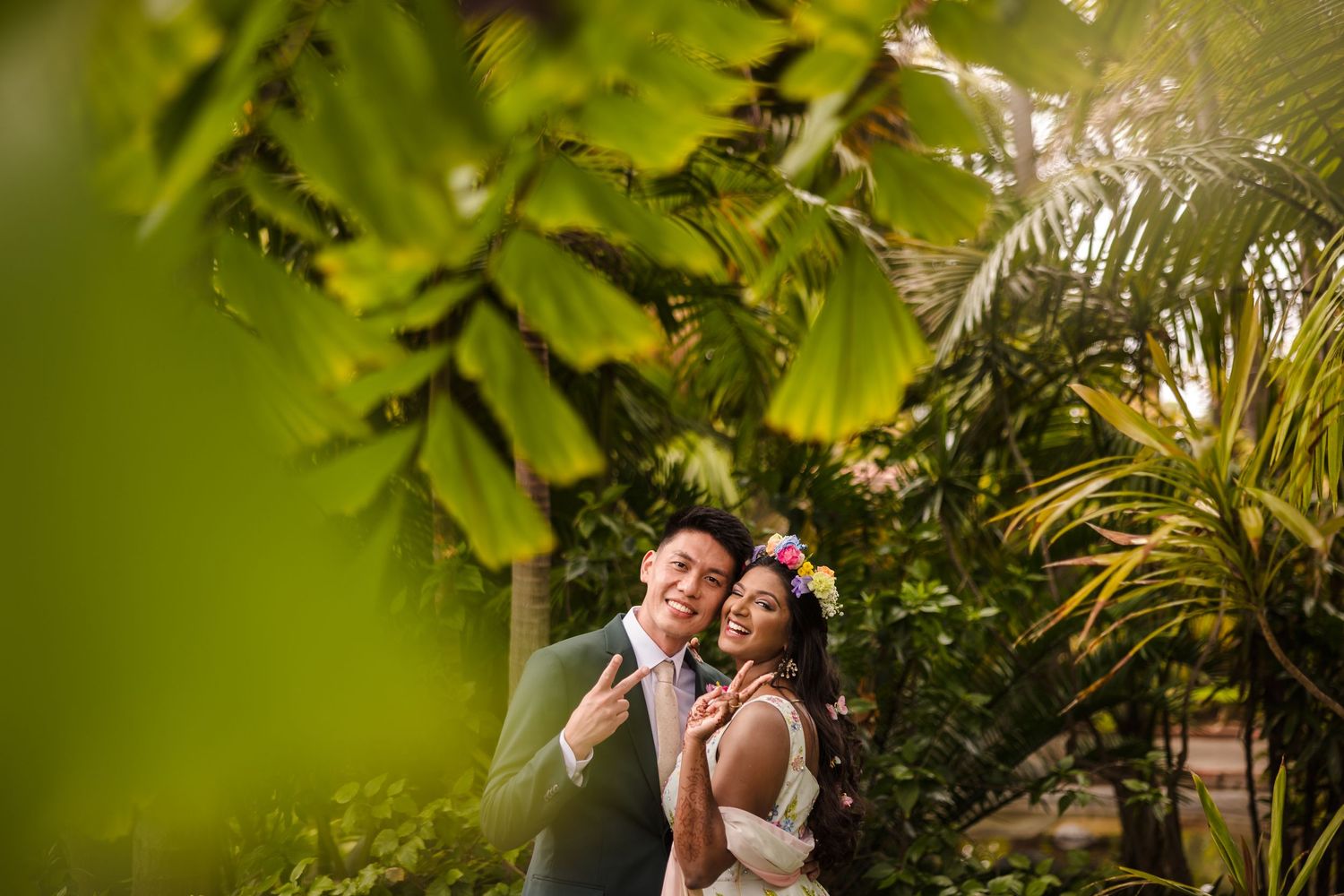 Wedding couple shares a joyful moment surrounded by lush tropical greenery and palm fronds during their special day.