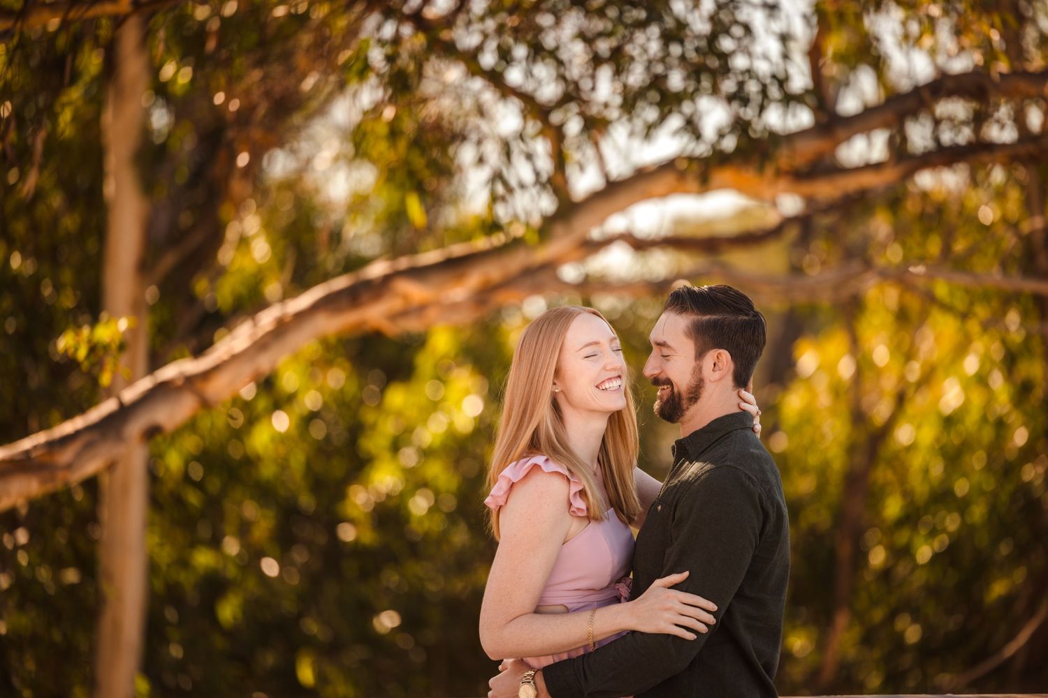A romantic couple embraces in soft golden sunlight under autumn trees during a sunset portrait session.