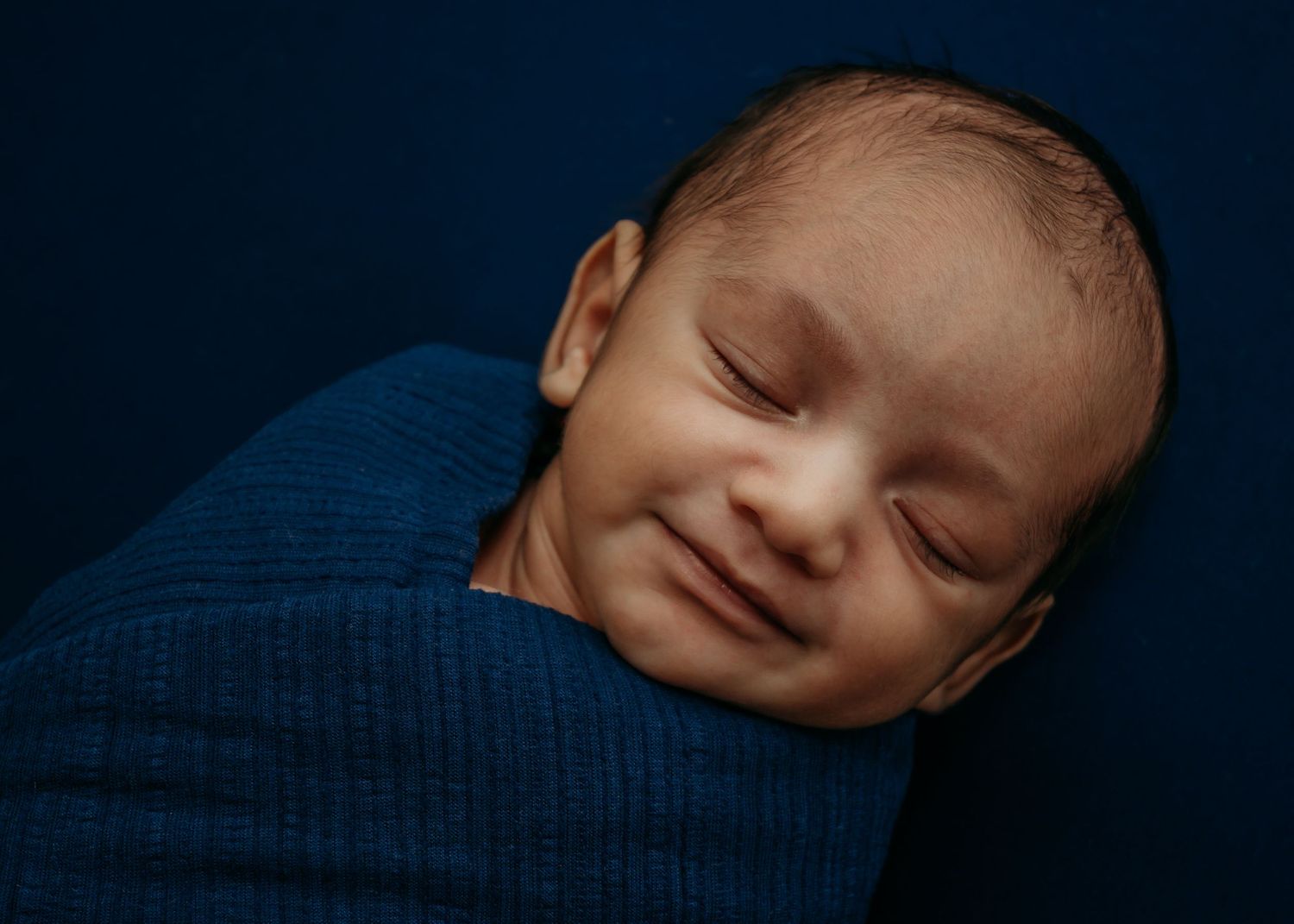 Newborn boy wrapped in blue with matching background