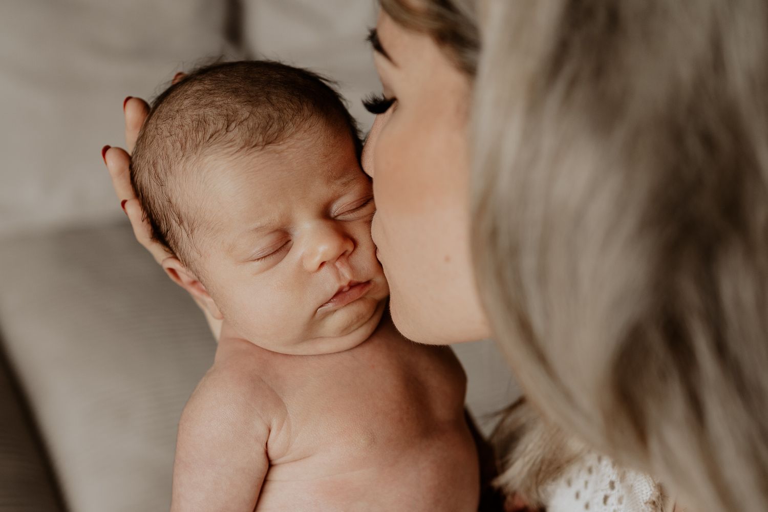 Natürliche Neugeborenenfotografie in Roth: Mutter küsst ihr neugeborenes Baby sanft auf die Wange, während es ruhig in ihren Händen liegt.