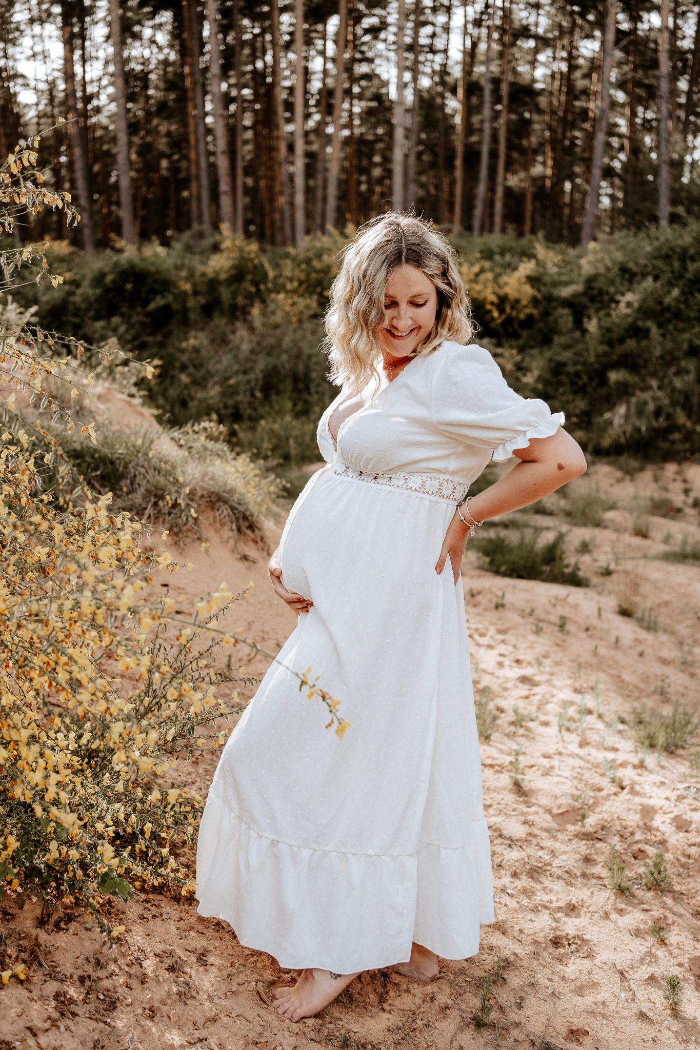 Schwangere Frau zeigt Babybauch bei entspanntem Fotoshooting im Freien.