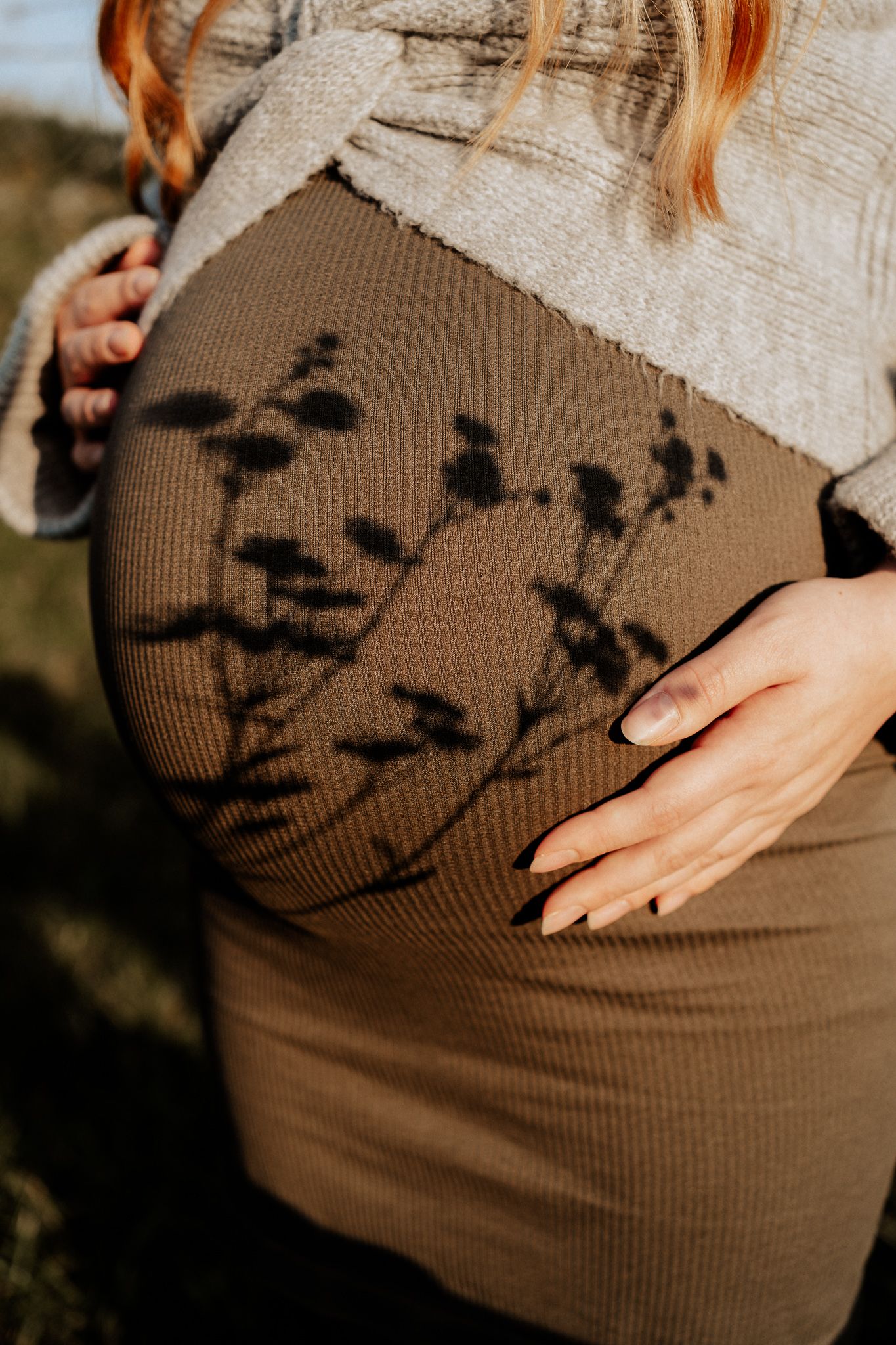 Babybauch mit natürlichen Pflanzenschatten bei einem künstlerischen Schwangerschaftsshooting im Freien.