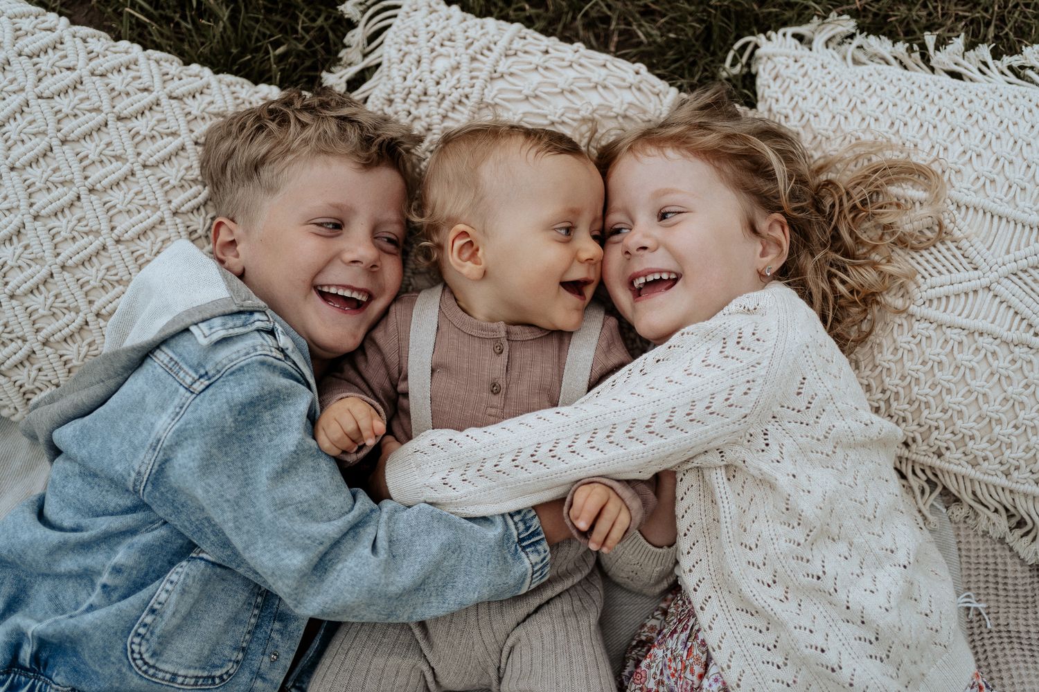 Liebevolle Geschwisterfotos mit drei Kindern, die eng beieinander liegen, kuscheln und gemeinsam lachen.