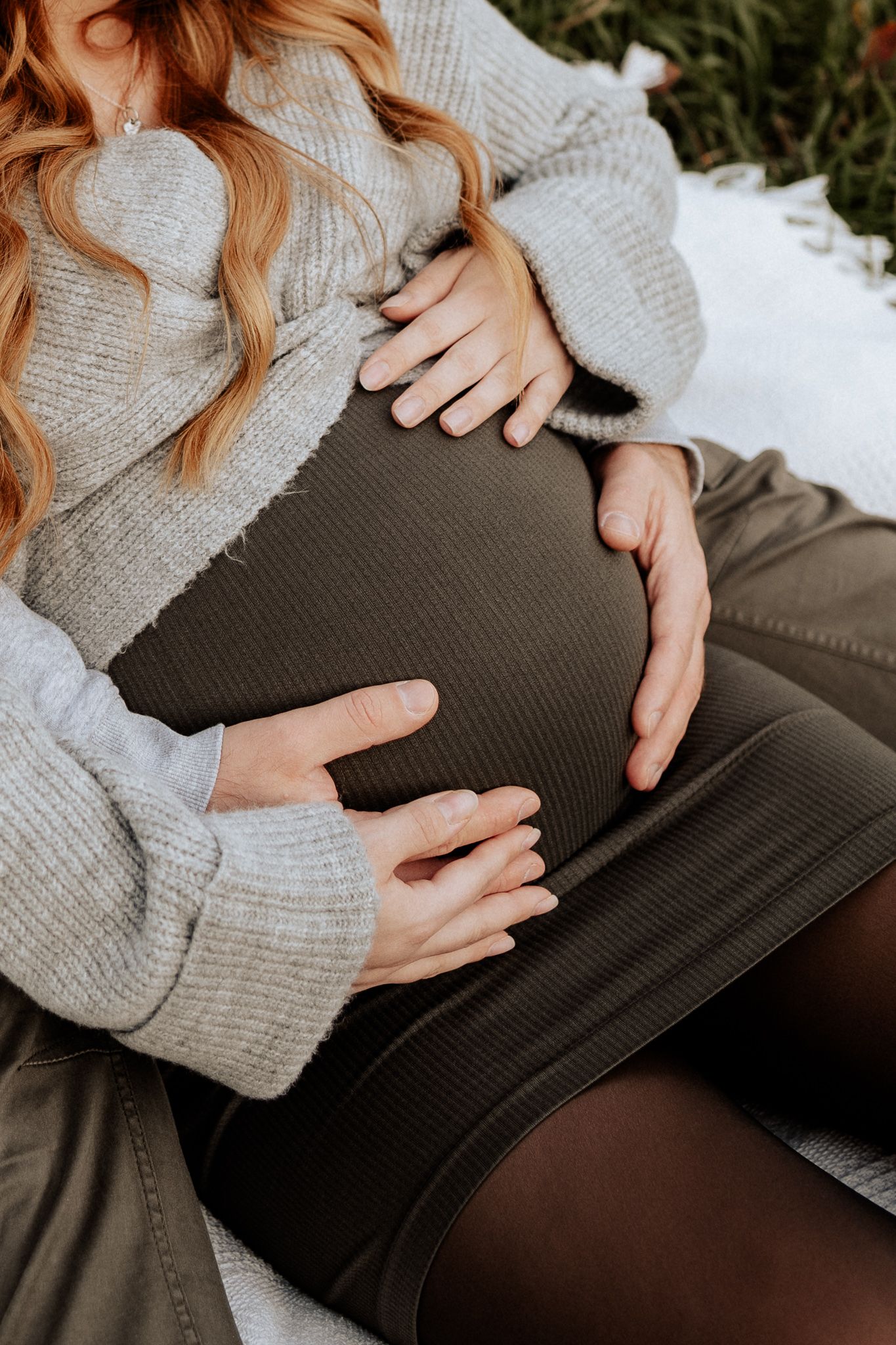 Nahaufnahme eines Babybauchs mit Händen der werdenden Eltern in entspannter Atmosphäre.