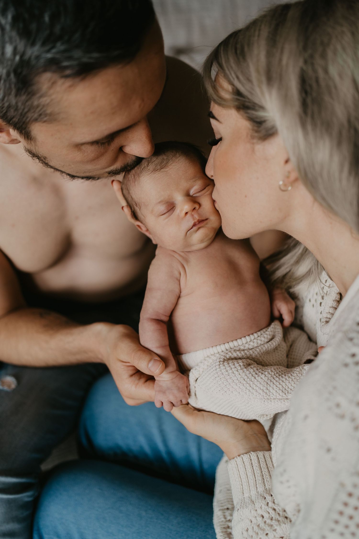 Neugeborenes Baby schläft in den Händen der Mutter und wird von ihr und dem Vater geküsst