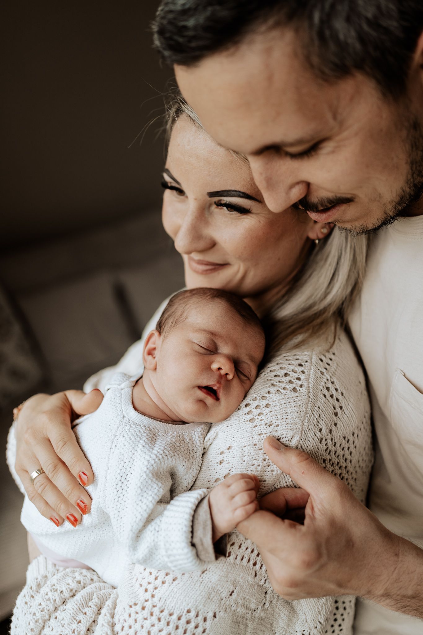 Natürliche Babyfotografie – Eltern kuscheln mit ihrem Neugeborenen in einem liebevollen, warmen Augenblick