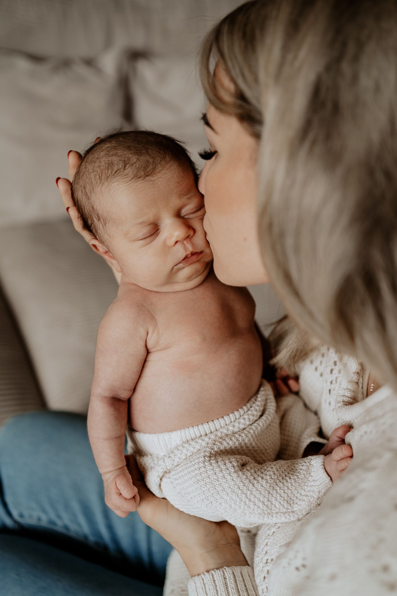 Mutter küsst ihr neugeborenes Baby sanft – ein Augenblick in ruhiger Atmosphäre.