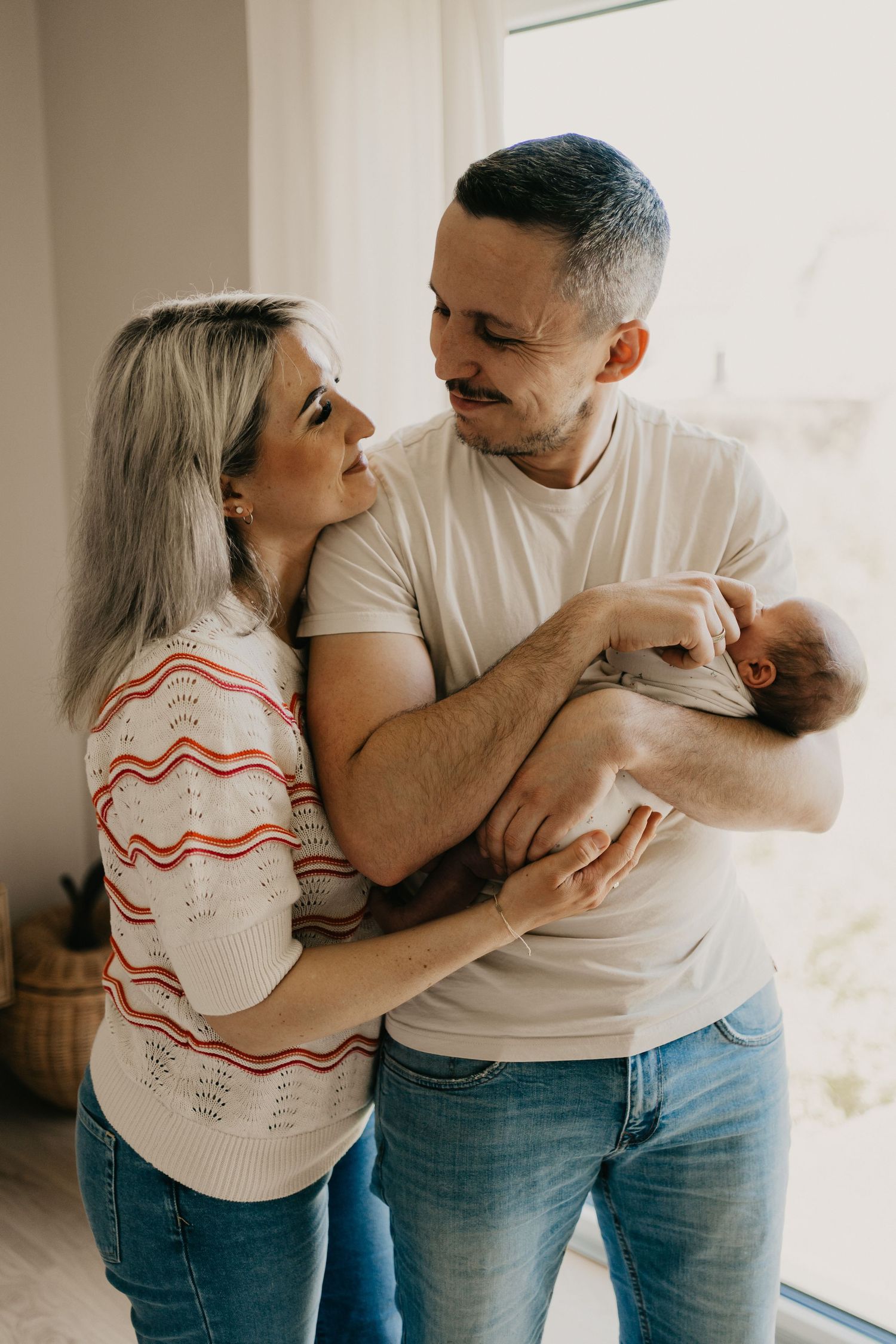 Eltern eines frisch geborenen Babys sehen sich glücklich in die Augen, während das neugeborene Baby auf dem Arm des Vaters schläft