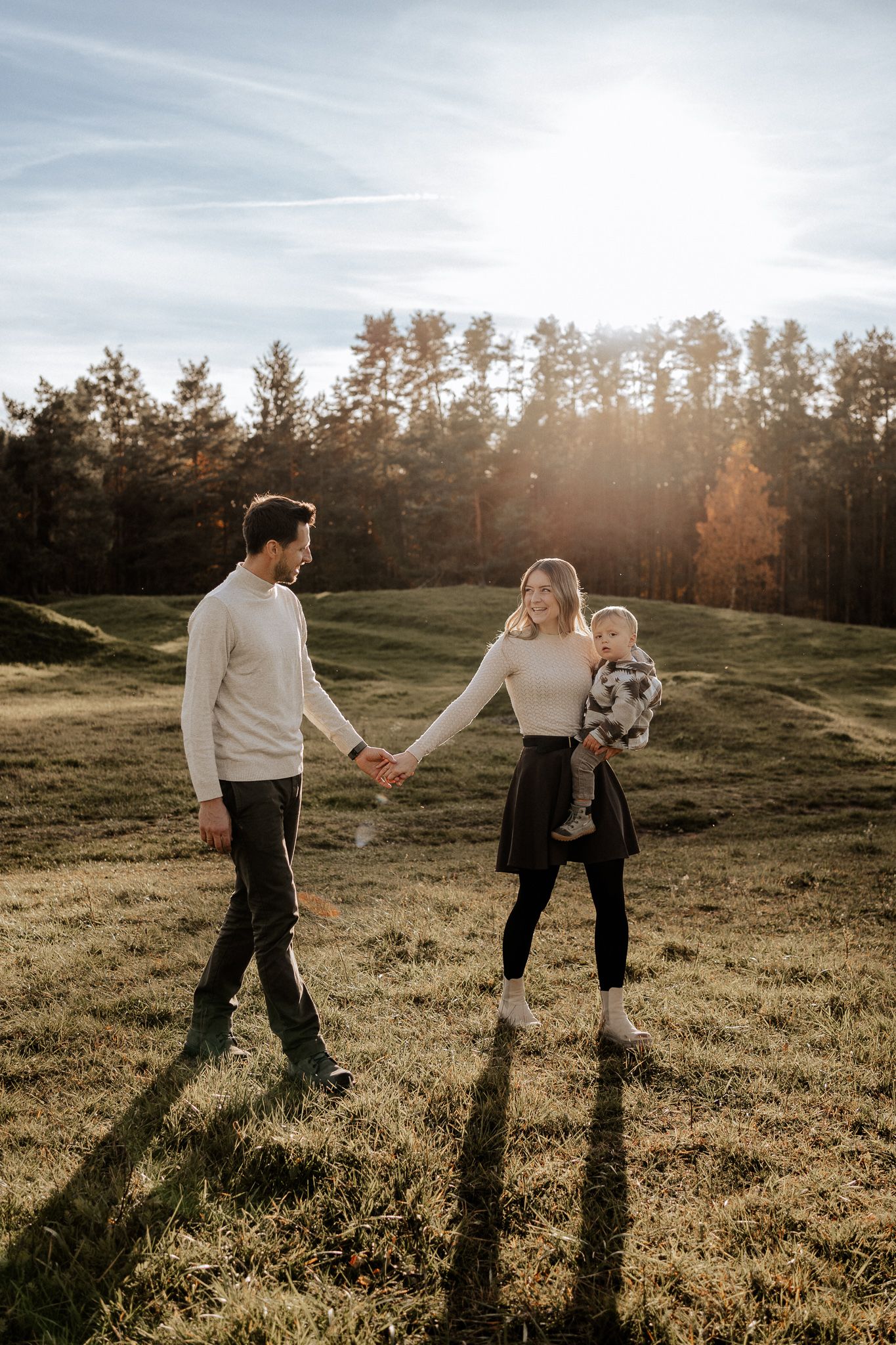 Eltern gehen Hand in Hand mit ihrem Kind durch die Natur – ruhiger Familienmoment im Abendlicht.