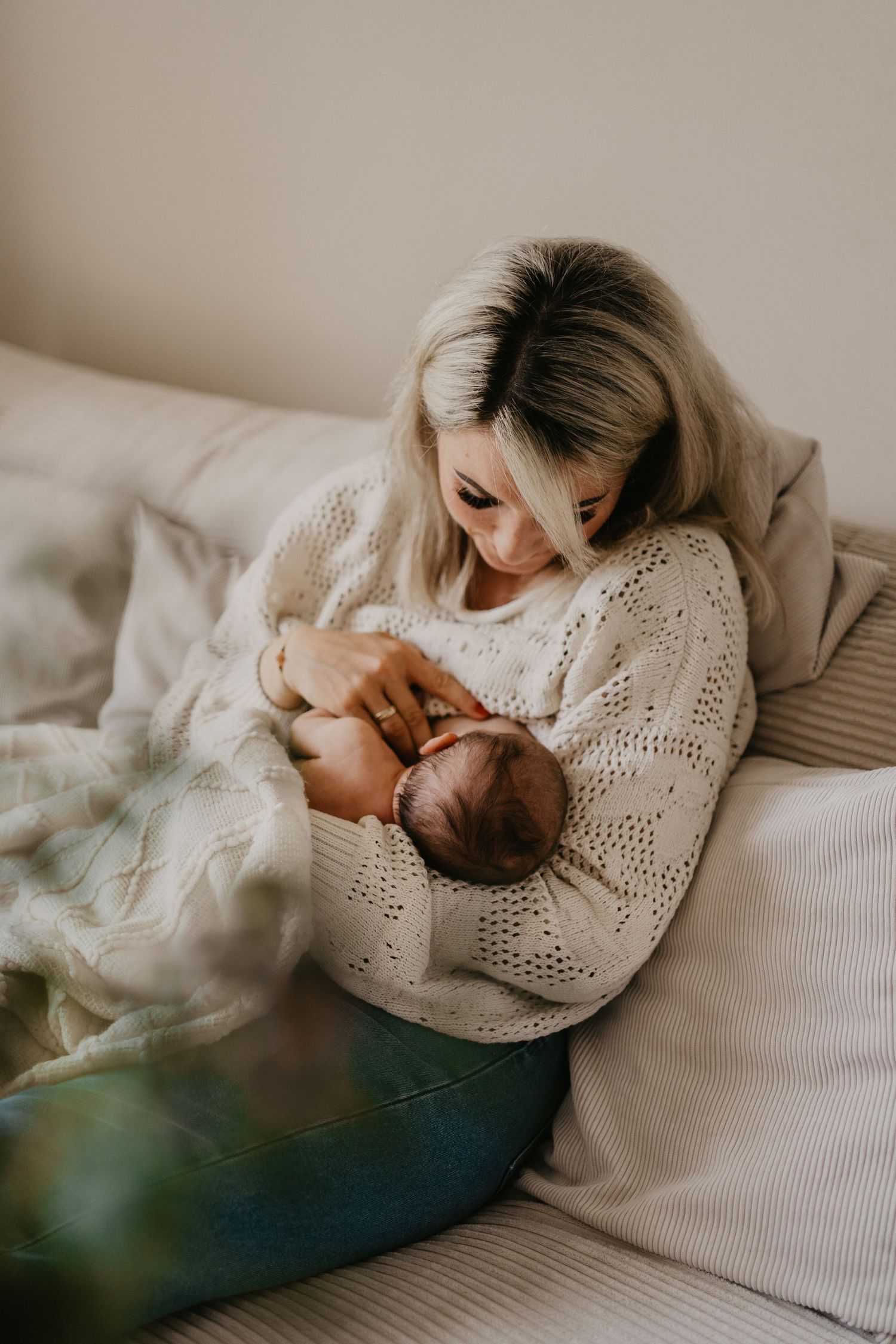 Mama sitzt gemütlich auf dem Sofa und stillt ihr neugeborenes Baby