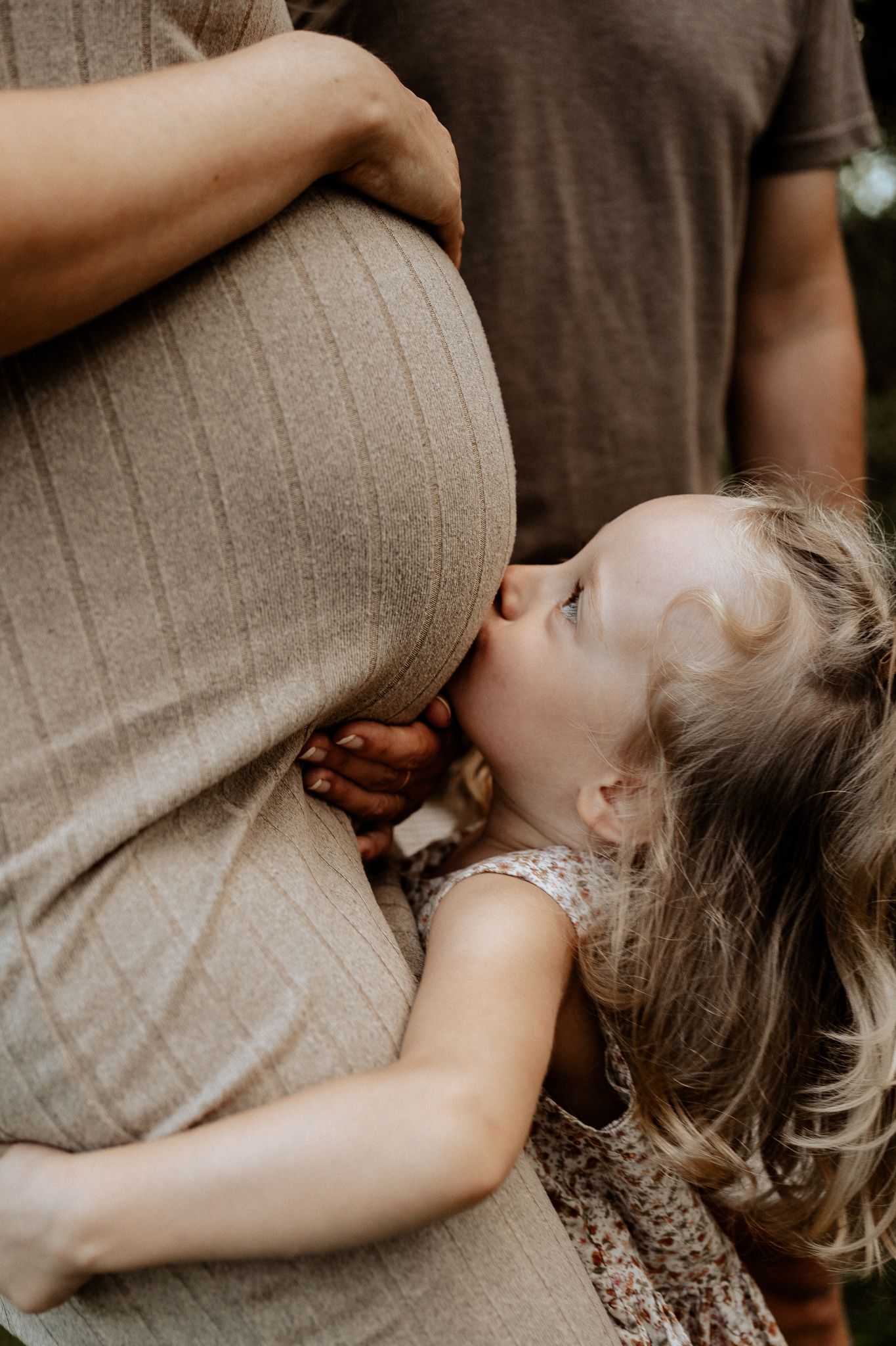 Liebevolle Familienszene, Kind küsst den Babybauch während eines Outdoor Schwangerschafts Shootings.