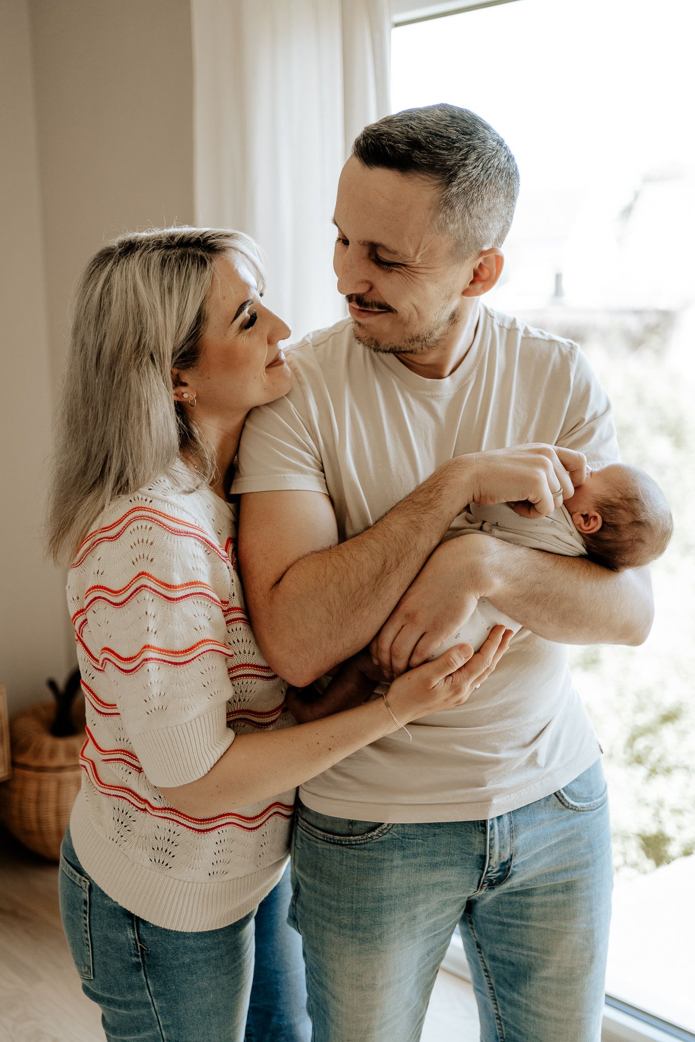 Eltern halten ihr Baby liebevoll im Arm und genießen die gemeinsame Zeit.