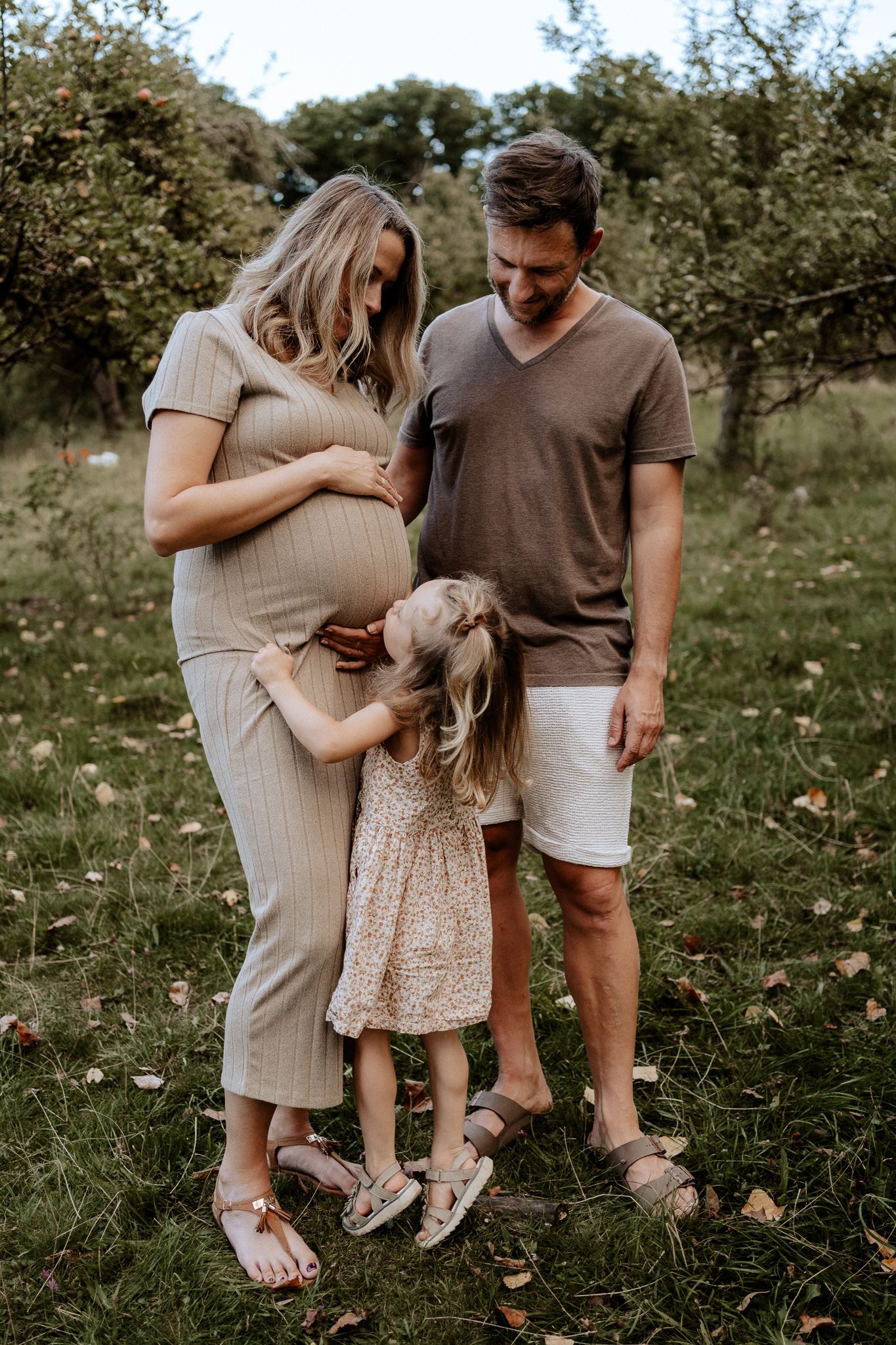 Familienshooting mit Babybauch in der Natur – Kind berührt liebevoll den Bauch der Mutter.