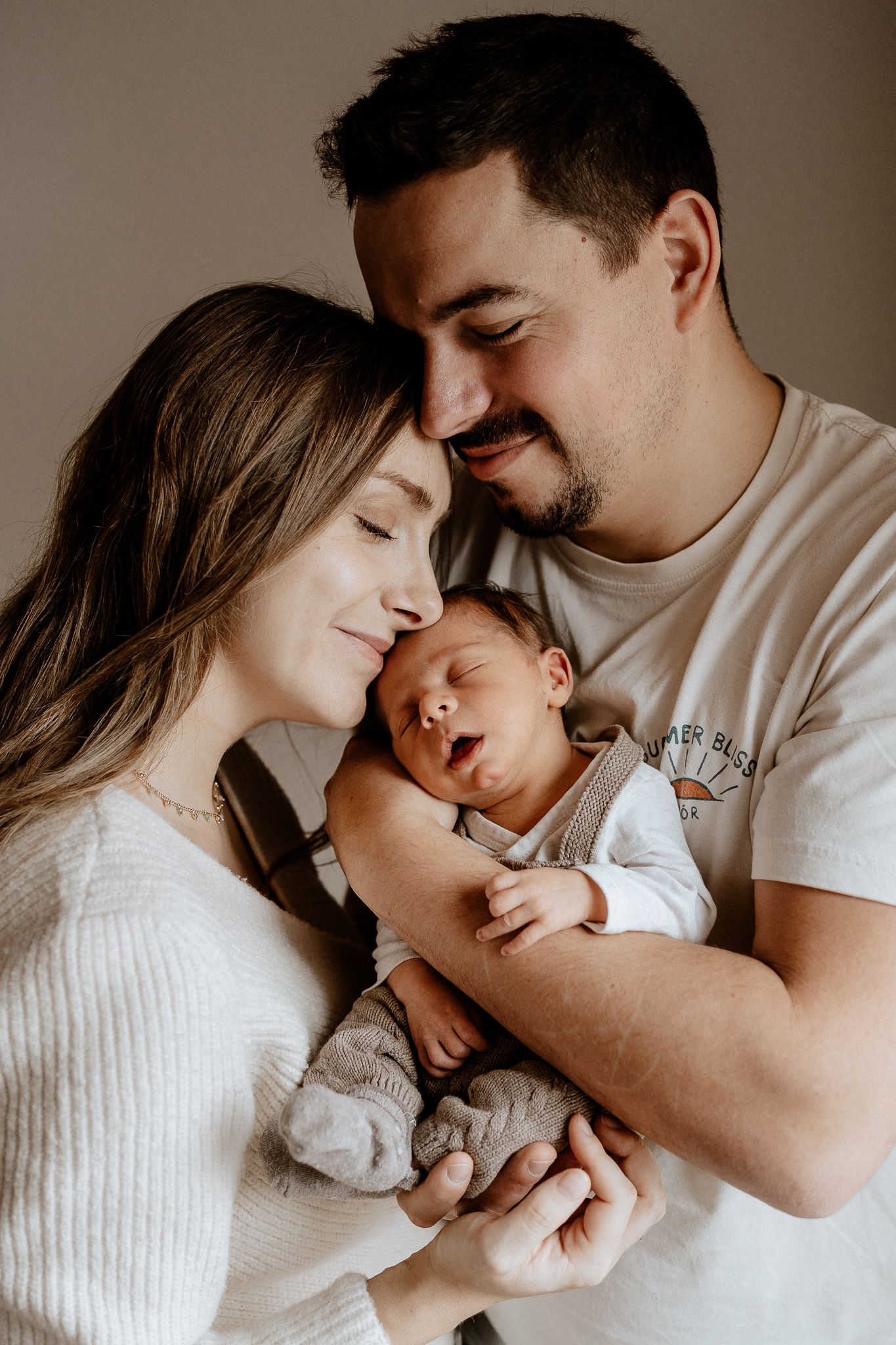 Eltern halten ihr schlafendes Baby nah bei sich und genießen einen innigen Moment voller Geborgenheit.