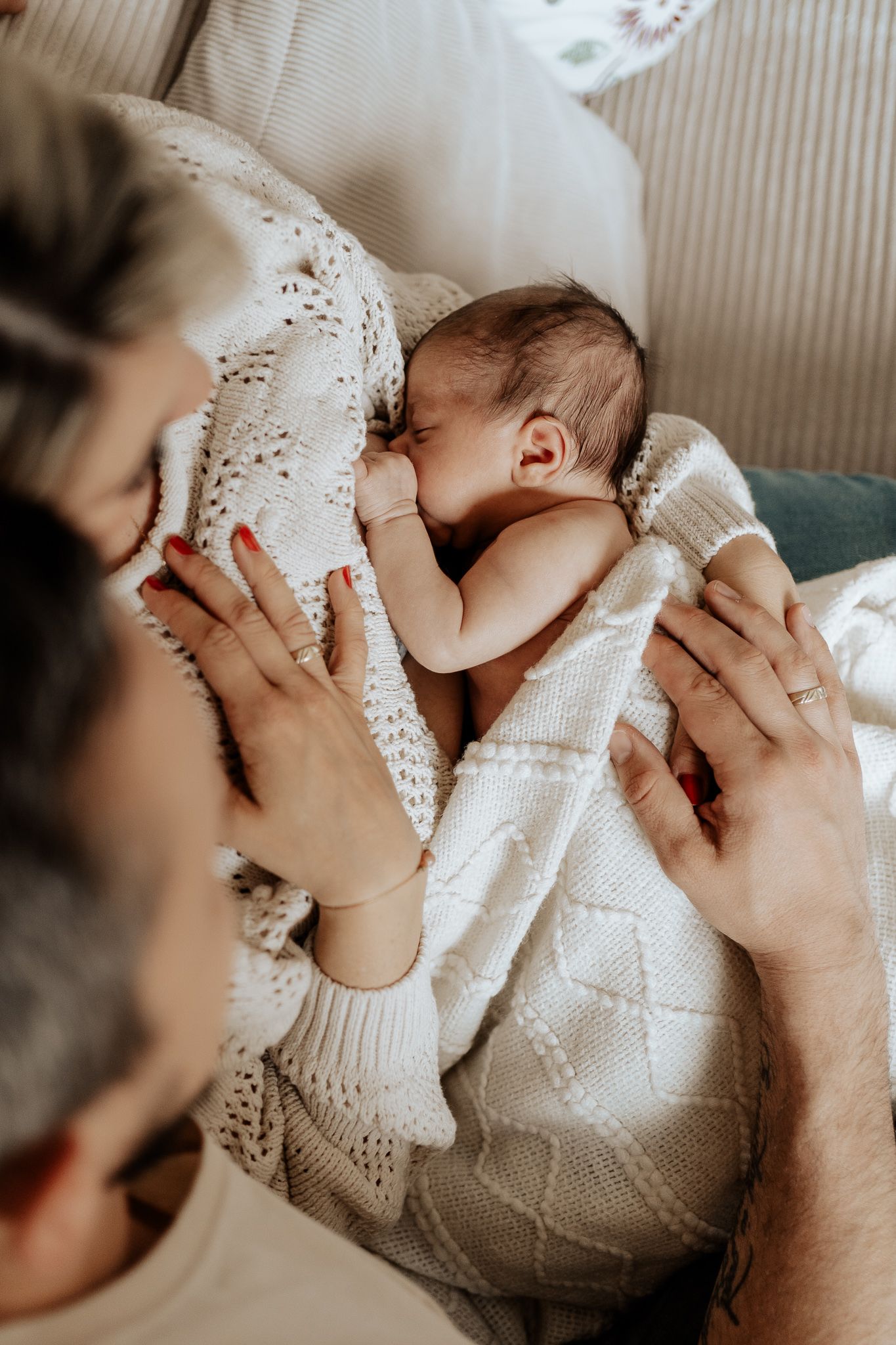 Intimer Stillmoment: Neugeborenes Baby liegt geborgen an der Brust seiner Mutter, während beide Eltern es liebevoll umgeben.