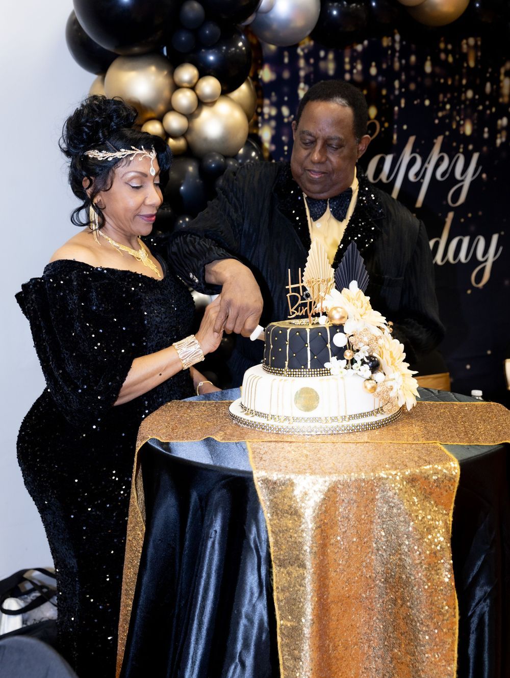Celebration event with elegant black and gold balloon decor and tiered cake.