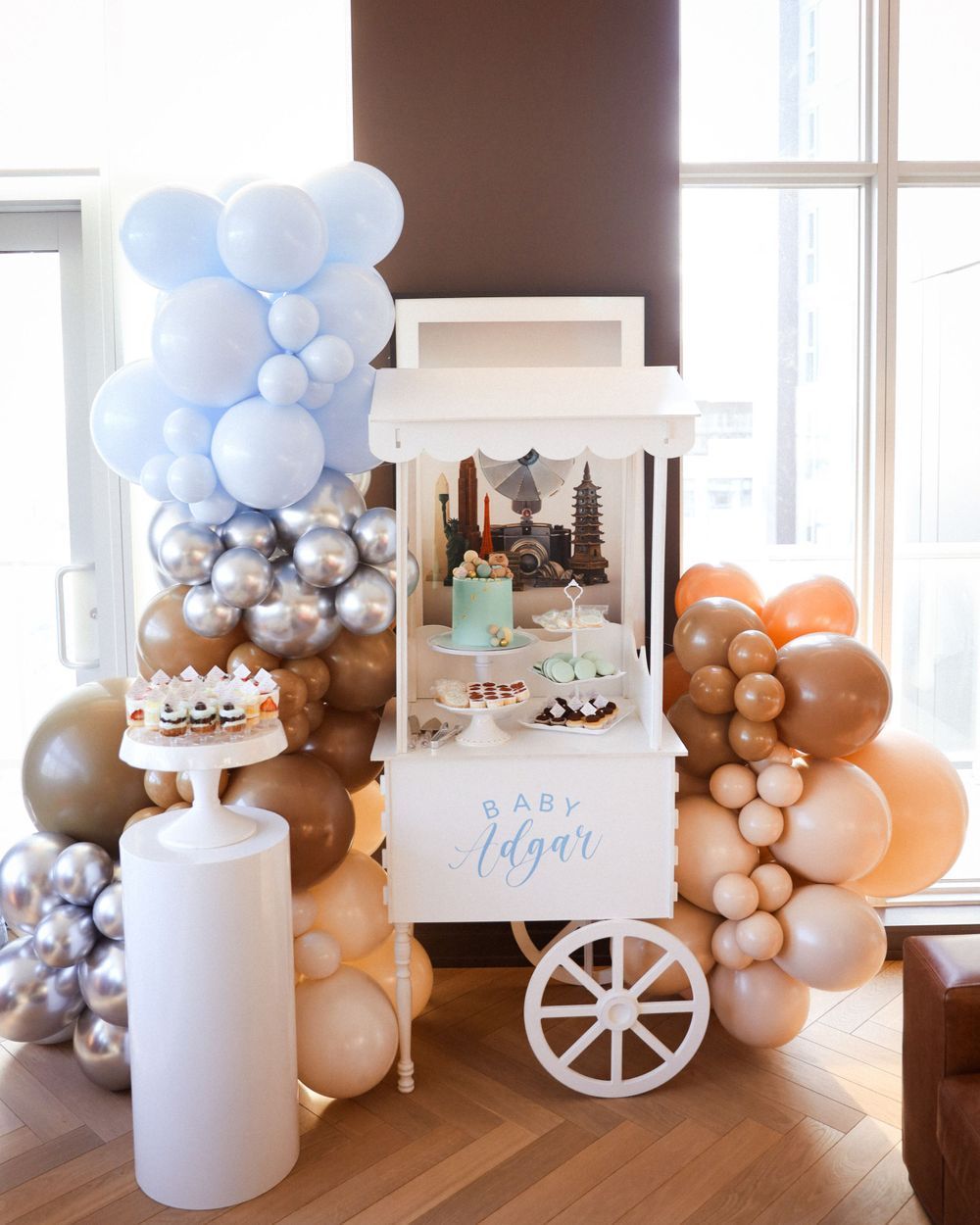 Elegant baby shower cart display with blue and peach balloon garland decorations and white accents.