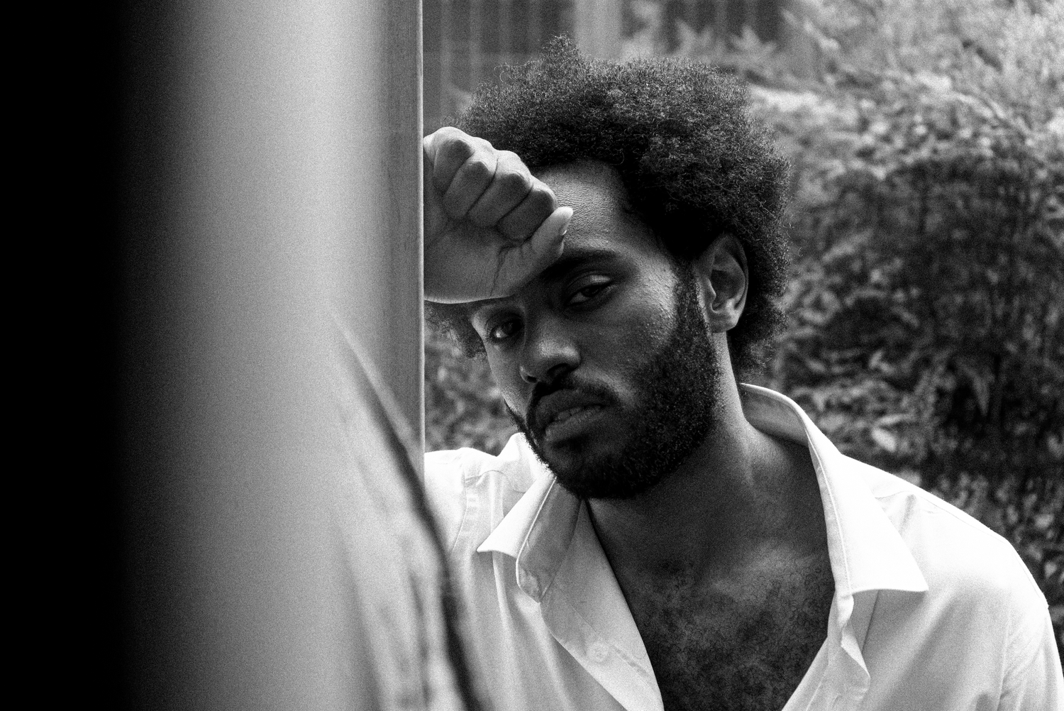 Black and white portrait of a thoughtful young man with an afro resting his hand on his forehead.