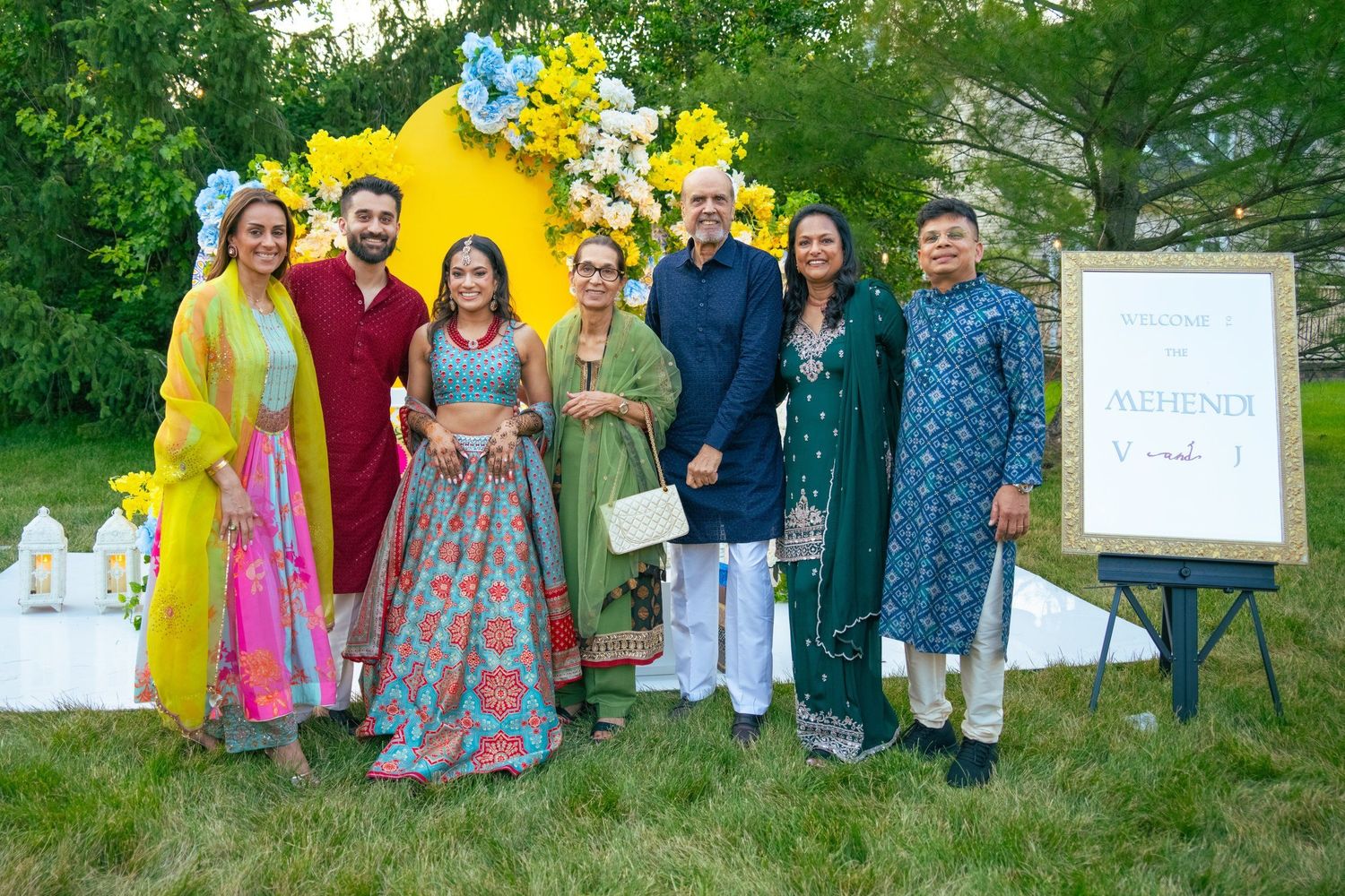 Group of seven people in colorful traditional Indian attire posing outdoors at a Mehndi celebration.