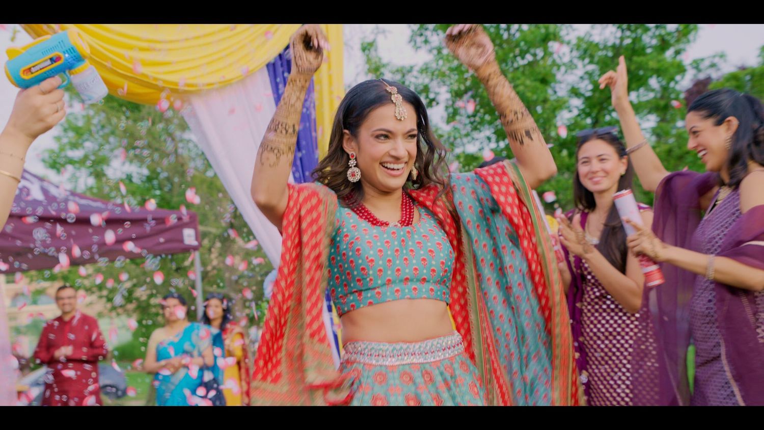 Woman in colorful lehenga dancing joyfully at vibrant Indian wedding celebration outdoors.