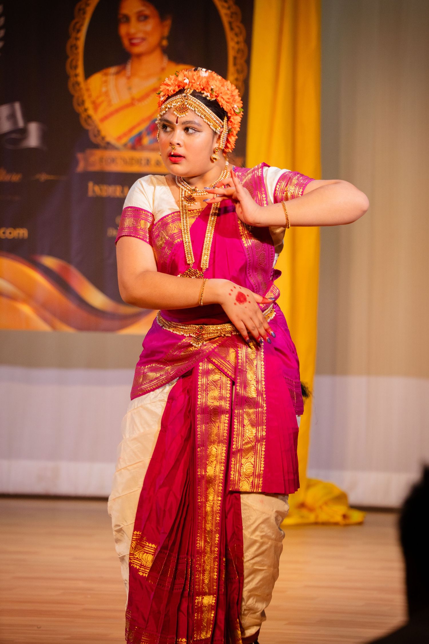 A woman performs Bharatanatyam dance in a traditional pink and gold silk saree with floral hair adornment.