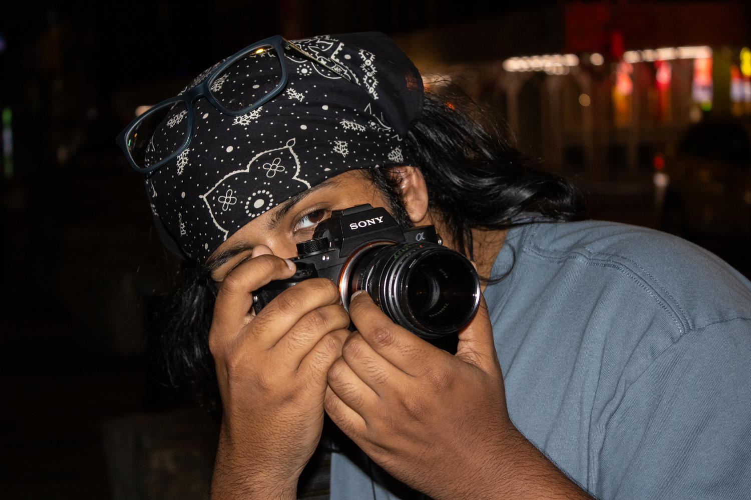 Photographer capturing photos at night with a Sony camera, wearing a black bandana head covering.