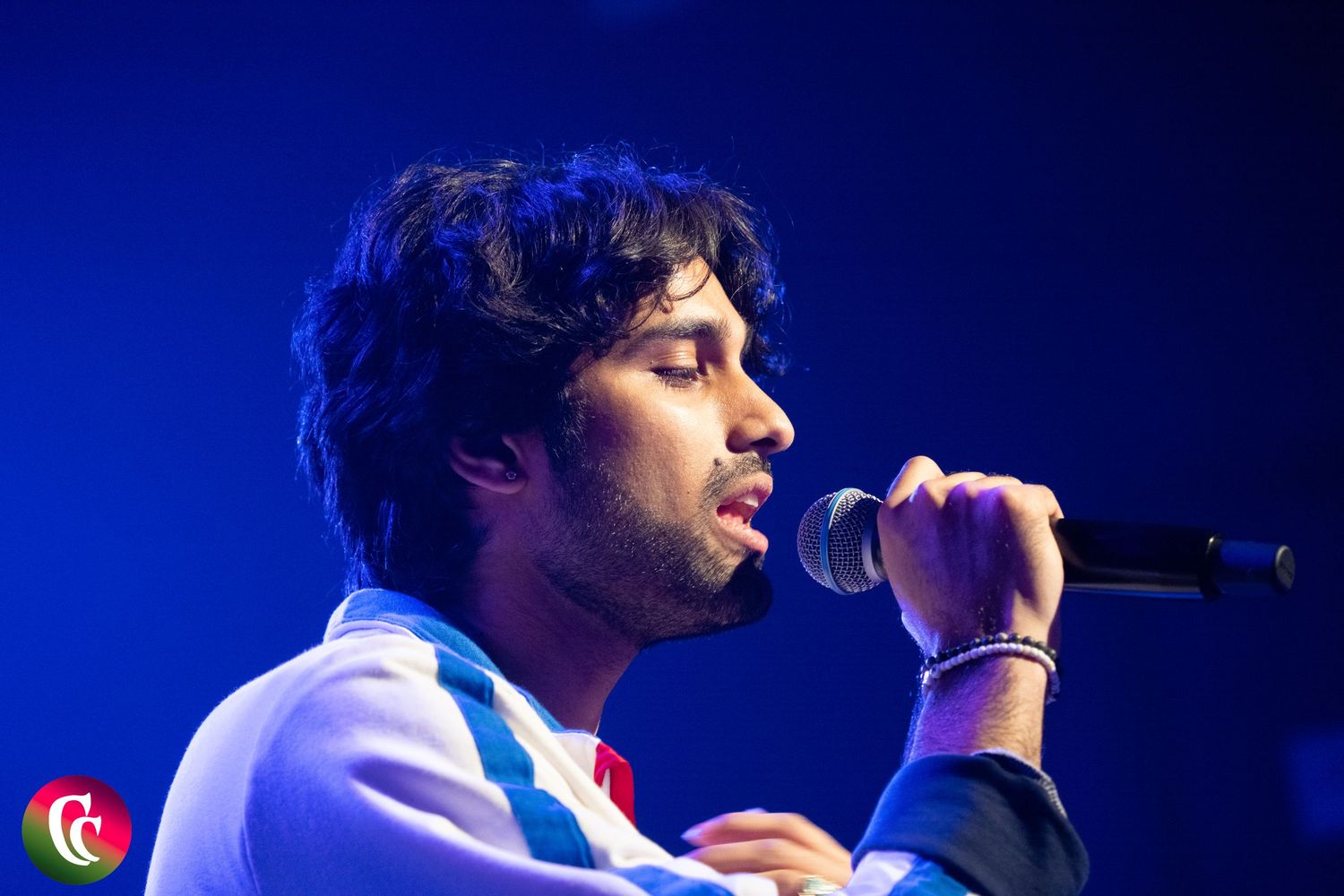 A young male singer with curly hair performs on stage under blue stage lighting holding a microphone.