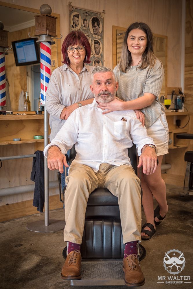 man in barber chair with two women standing