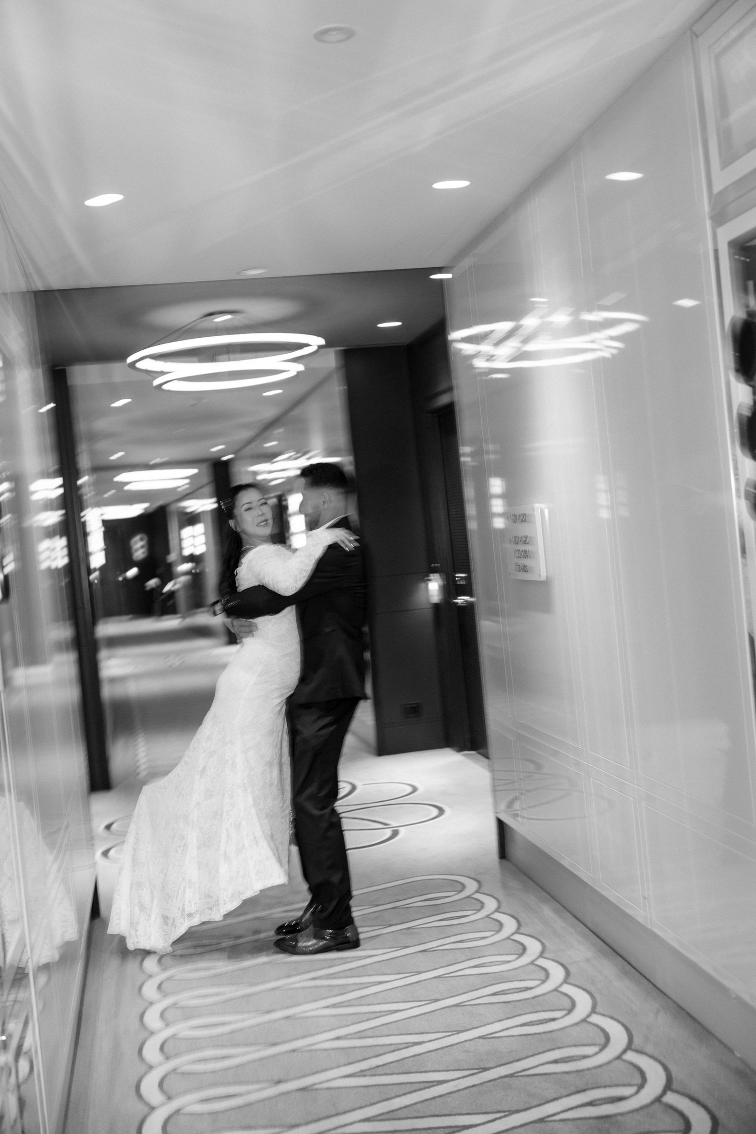 Black and white photo of bride and groom embracing in elegant hotel corridor on their wedding day.