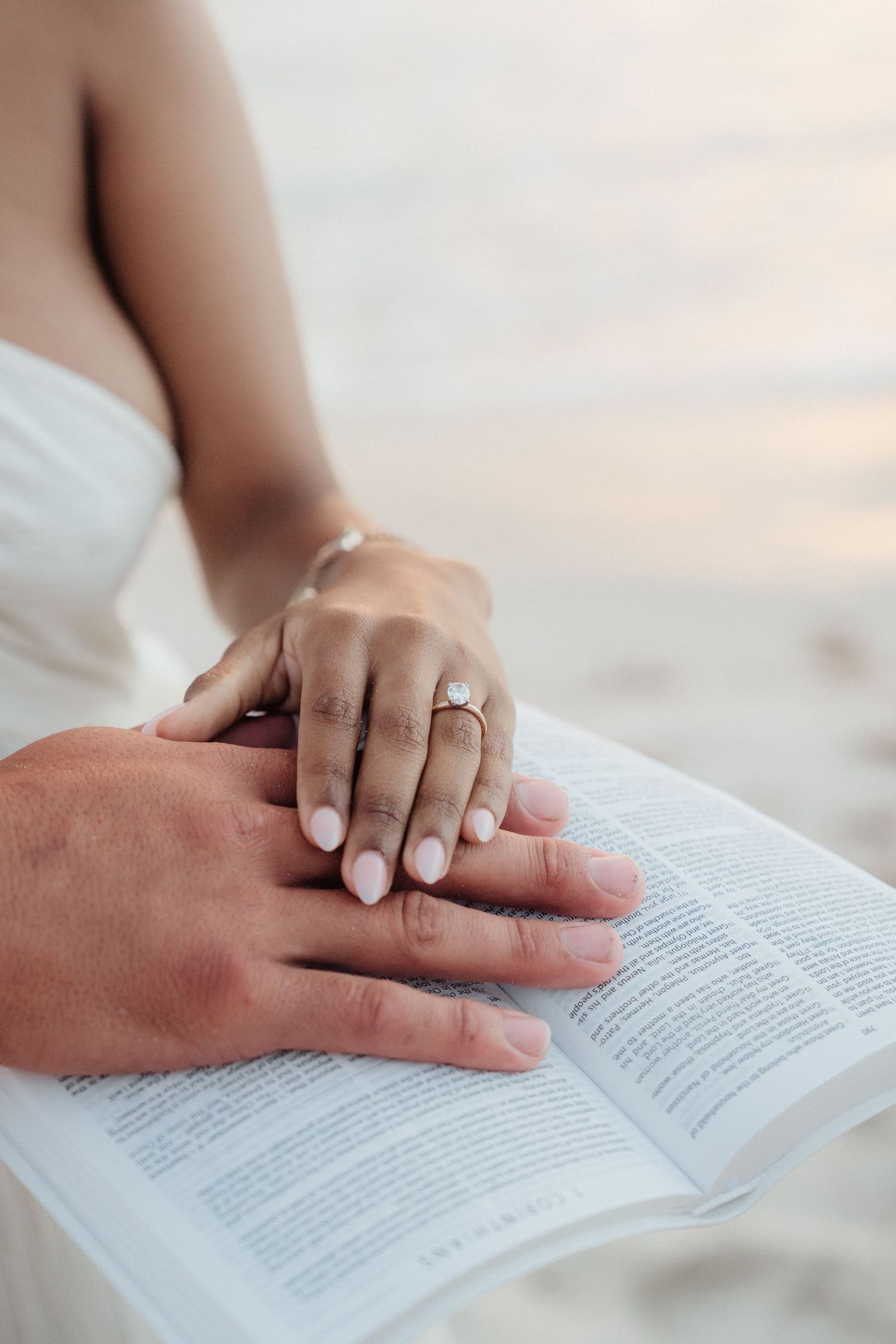 Newly engaged couple placing hands on open Bible, woman wearing diamond engagement ring.