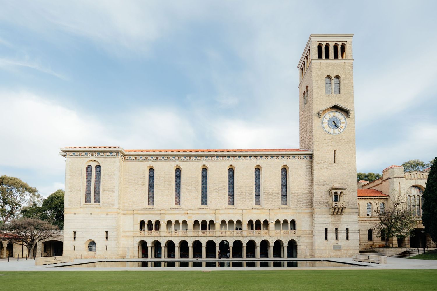 Historic university building with a clock tower, arched colonnades, and manicured lawn.