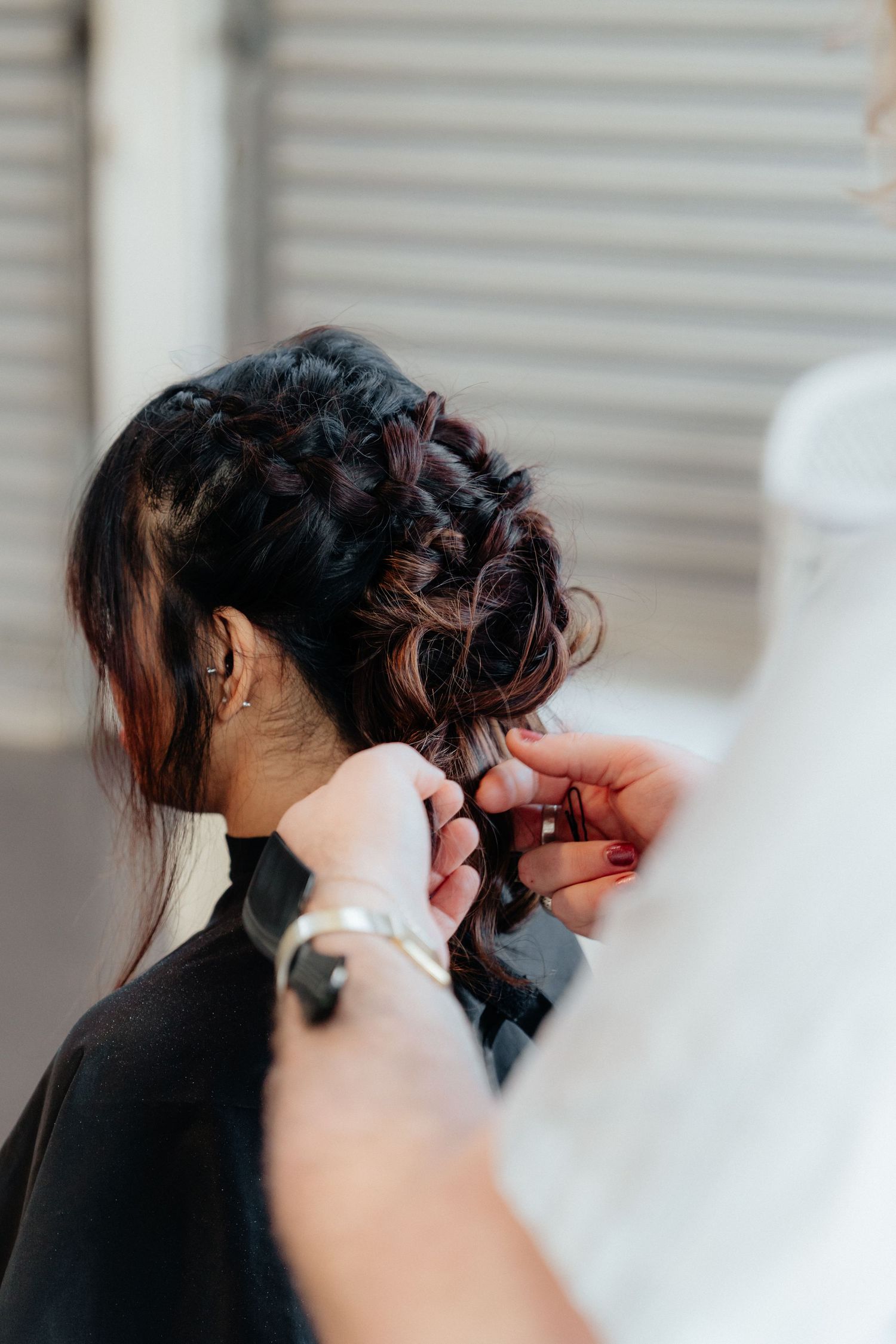 Hairstylist pinning an elegant braided updo on a dark-haired bride before her wedding.