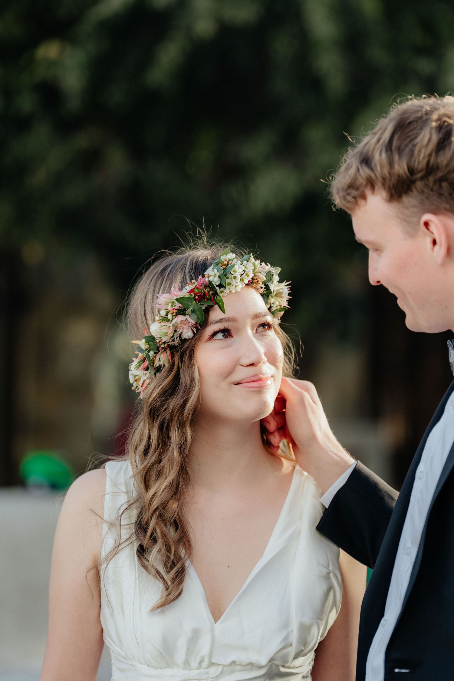 Groom tenderly touching bride's face as she smiles, bride wearing a beautiful floral flower crown.