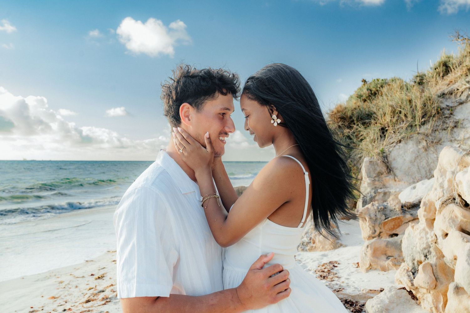 Romantic couple embracing face to face on a sunny beach with ocean in background.