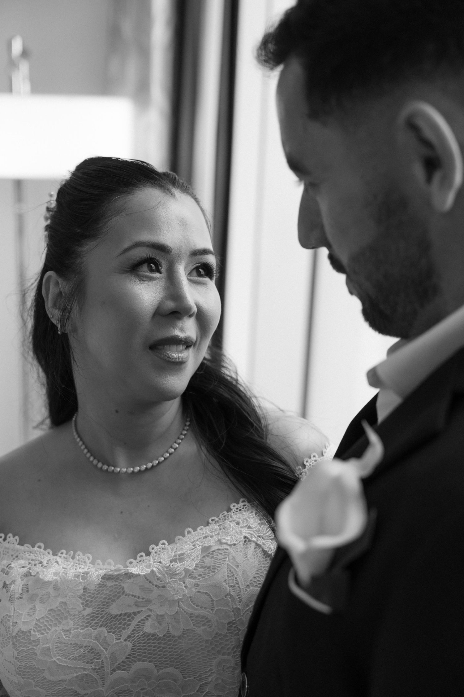Black and white portrait of bride in lace gown gazing lovingly at groom during intimate wedding moment.