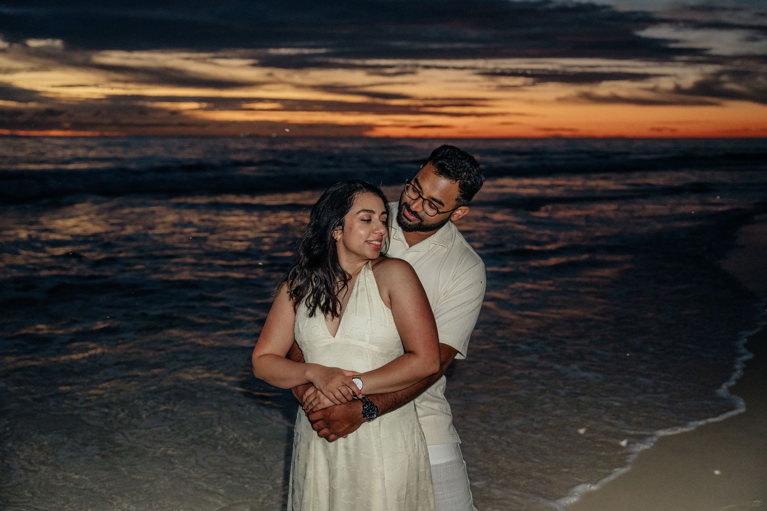 Couple sharing a warm embrace on the beach during a vibrant colorful sunset.